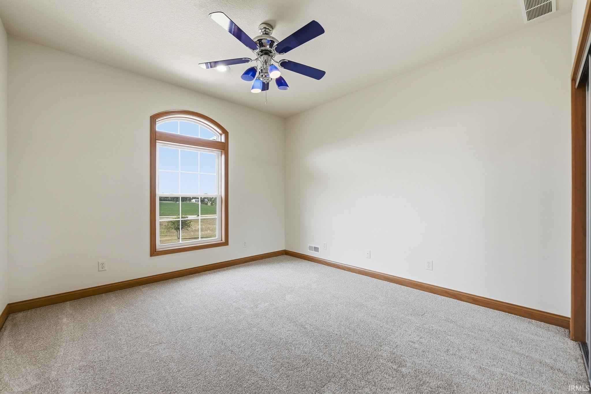 Room featuring an arched window with wood-finish trim, a ceiling fan with blue blades, light grey carpet flooring, and white walls