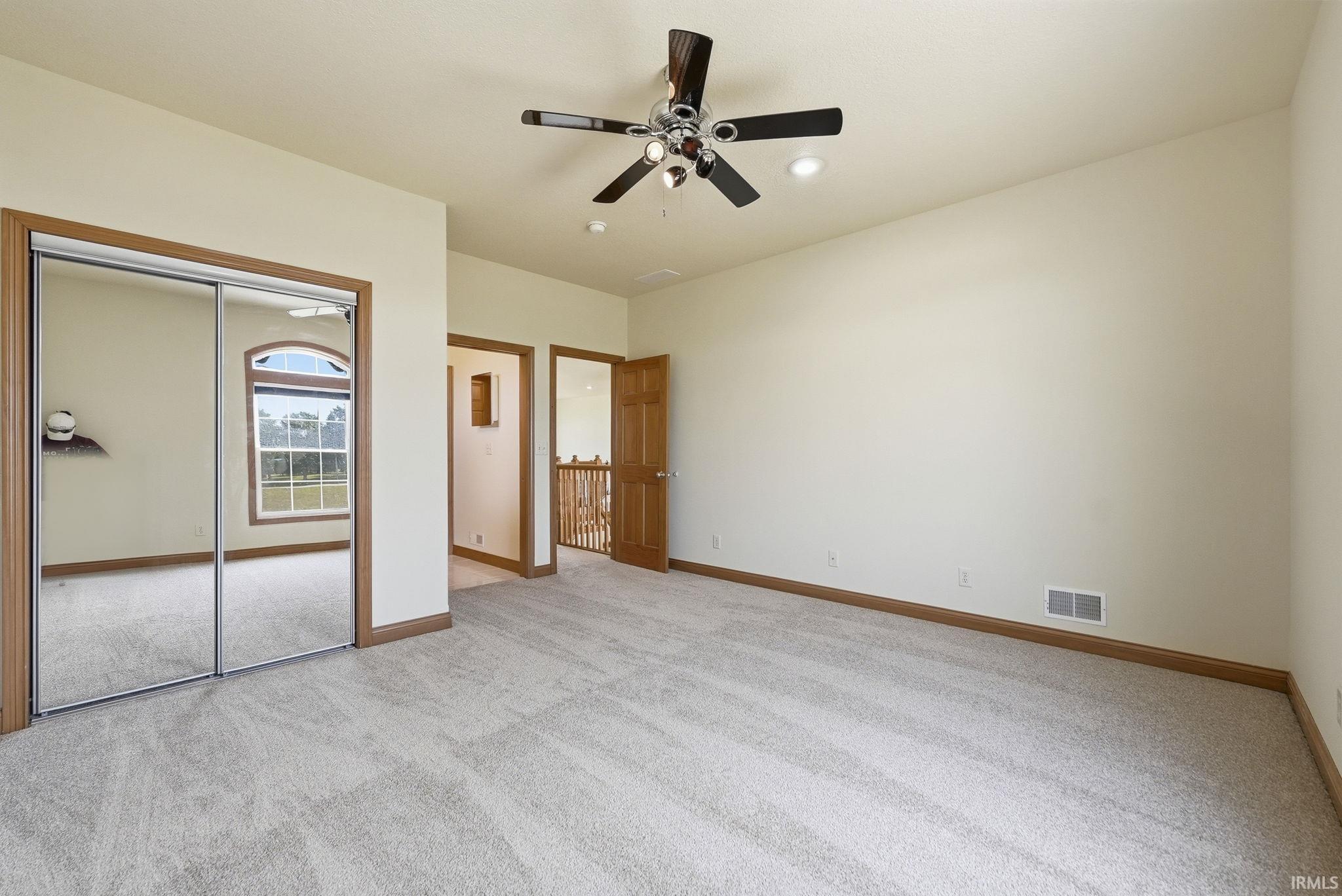Spacious room featuring light-toned carpet flooring, a ceiling fan with integrated lighting, and multiple wood-trimmed doorways