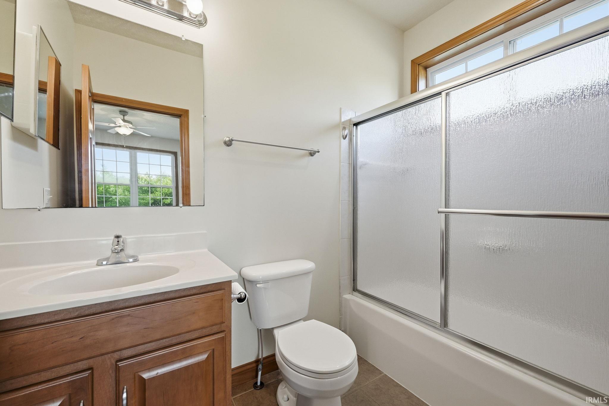 Bathroom featuring a wood-finish vanity with a white countertop, a mirror, and a shower-over-tub with frosted glass sliding doors