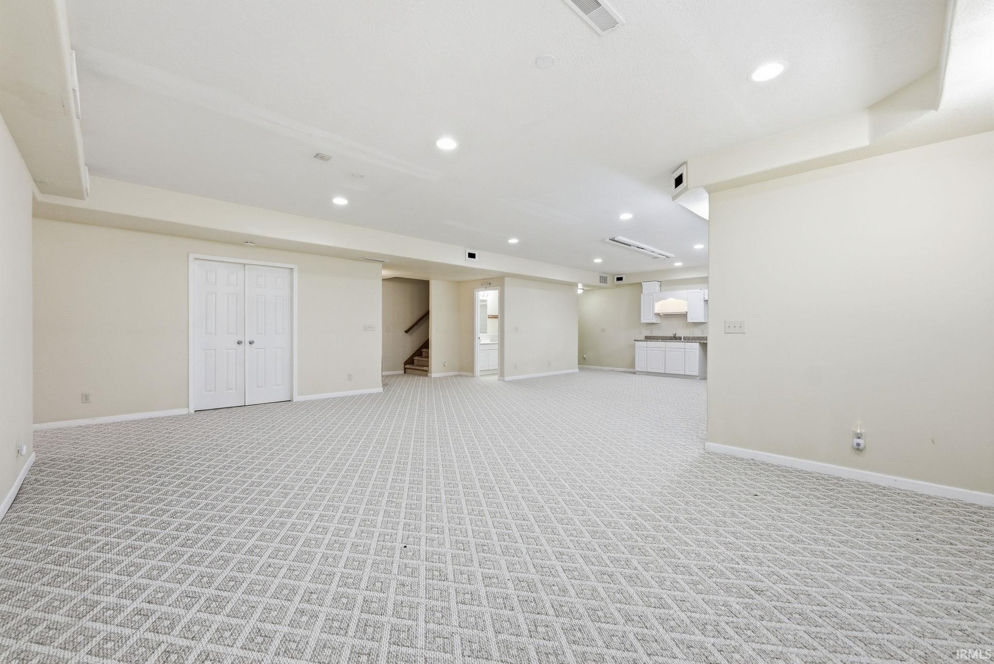 Spacious lower-level area with patterned carpet flooring, recessed lighting, and a neutral color palette