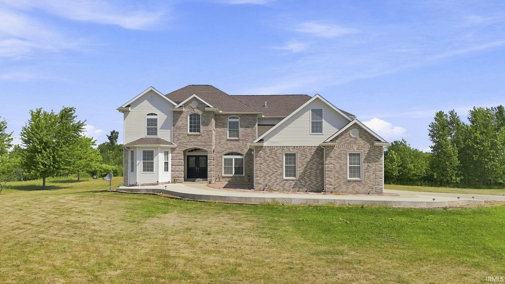 Two-story residence featuring a brick and siding exterior, arched windows, a multi-pane front door, and an expansive front lawn