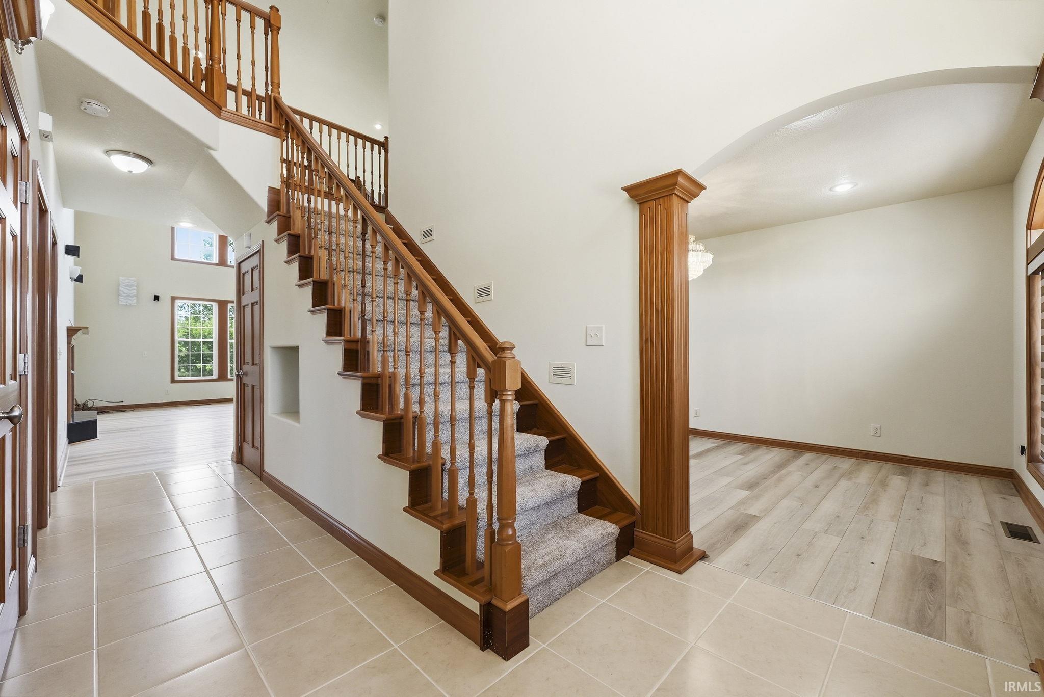 Grand foyer featuring a two-story staircase with wood balusters and carpeted treads, tile flooring, and a decorative column