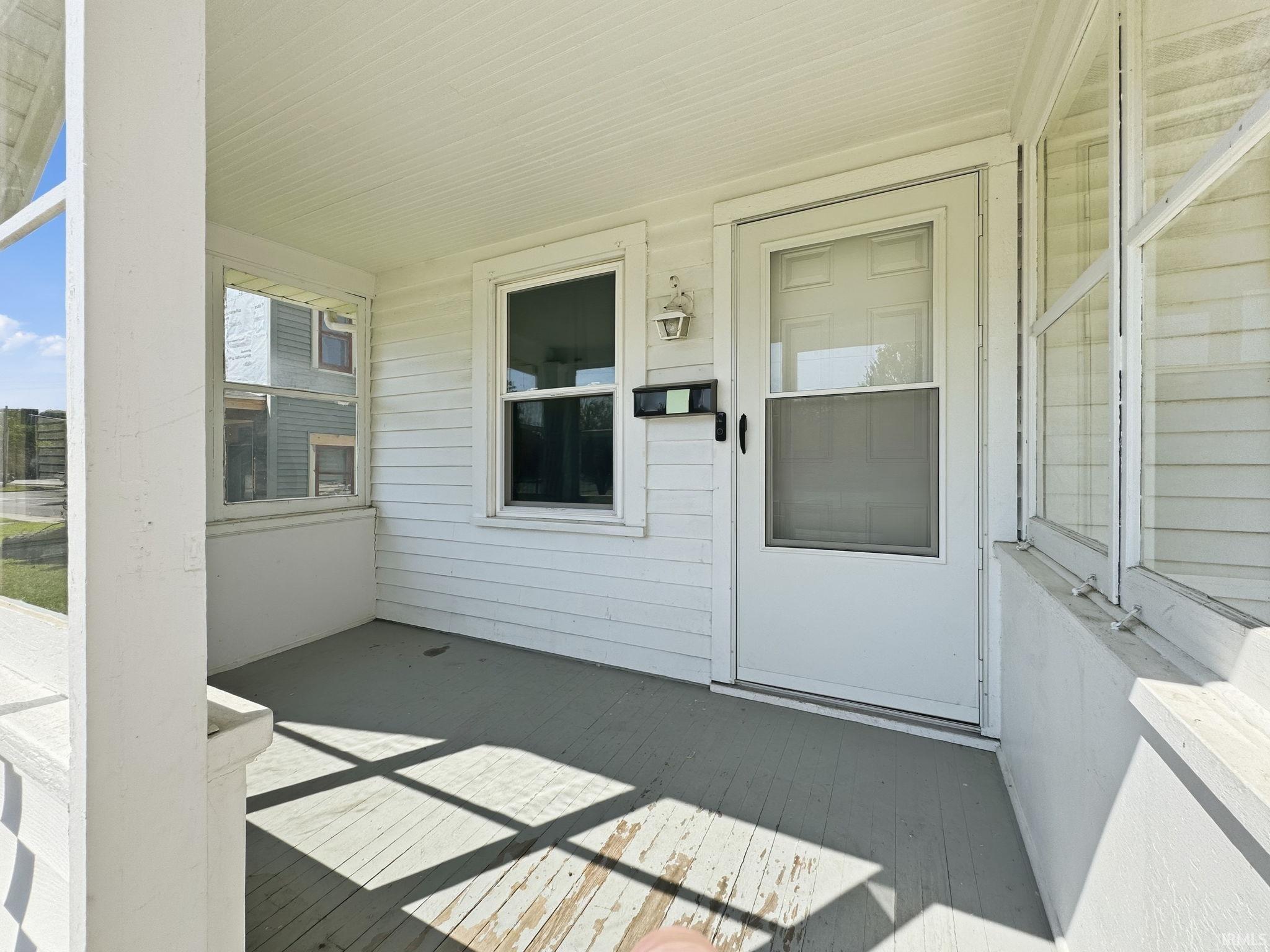 Covered porch entrance featuring white clapboard siding and a white paneled door with a screen insert