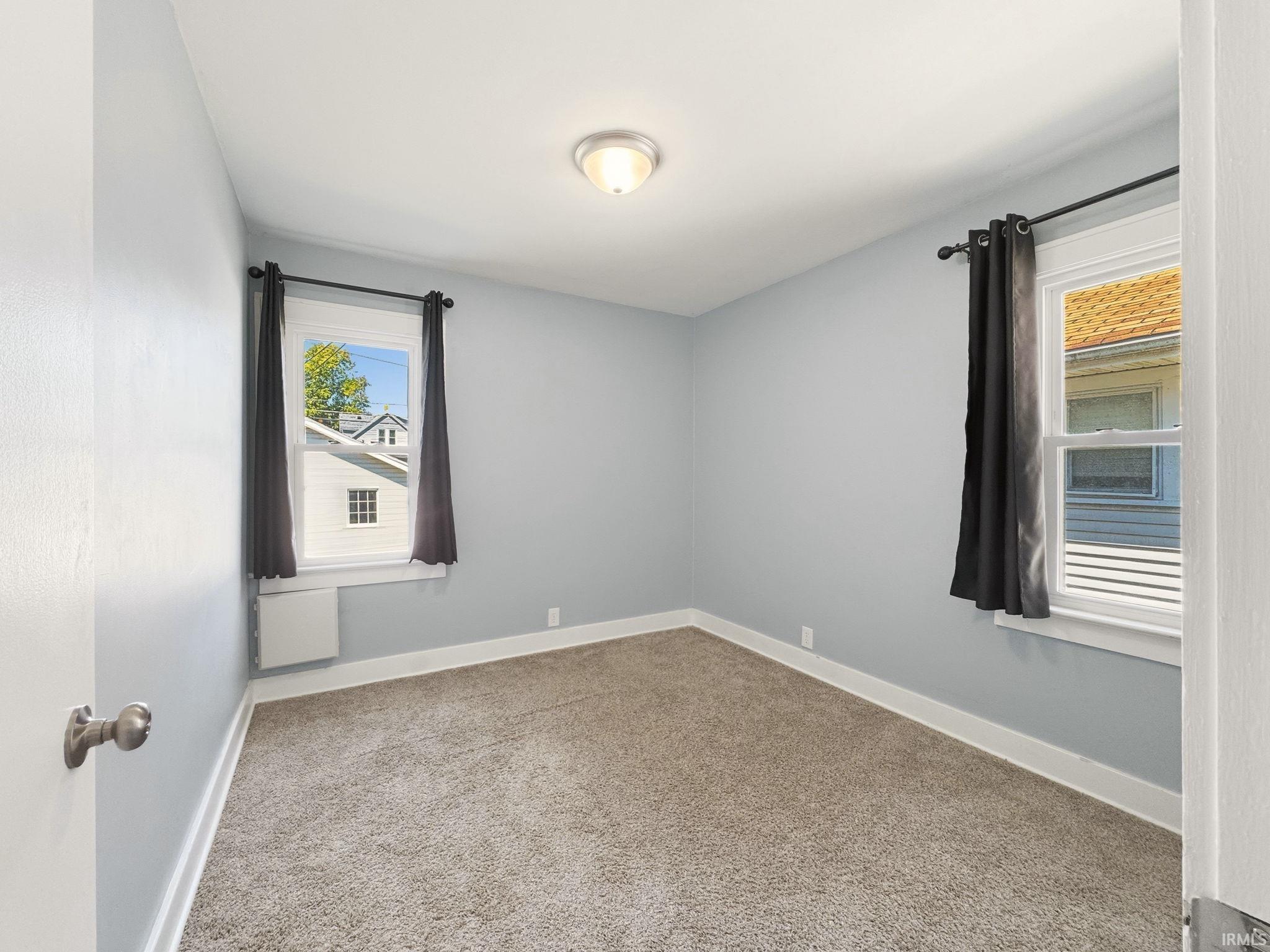 Carpeted room featuring light gray walls, white trim, and two windows with dark curtain rods