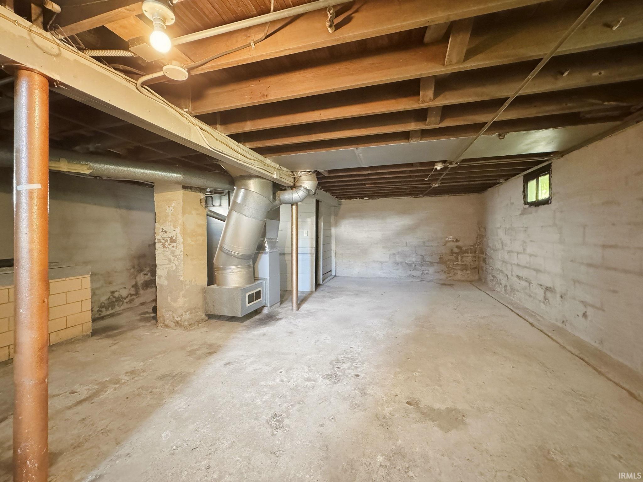 Unfinished basement with concrete flooring, exposed wood beam ceiling, and a visible window