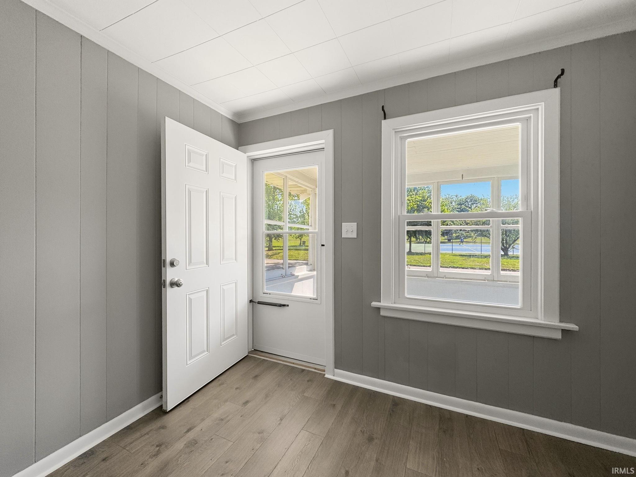 Entryway featuring wood-finish flooring, vertical paneling, a paneled door with partial light, and a single-hung window with a water feature visible beyond