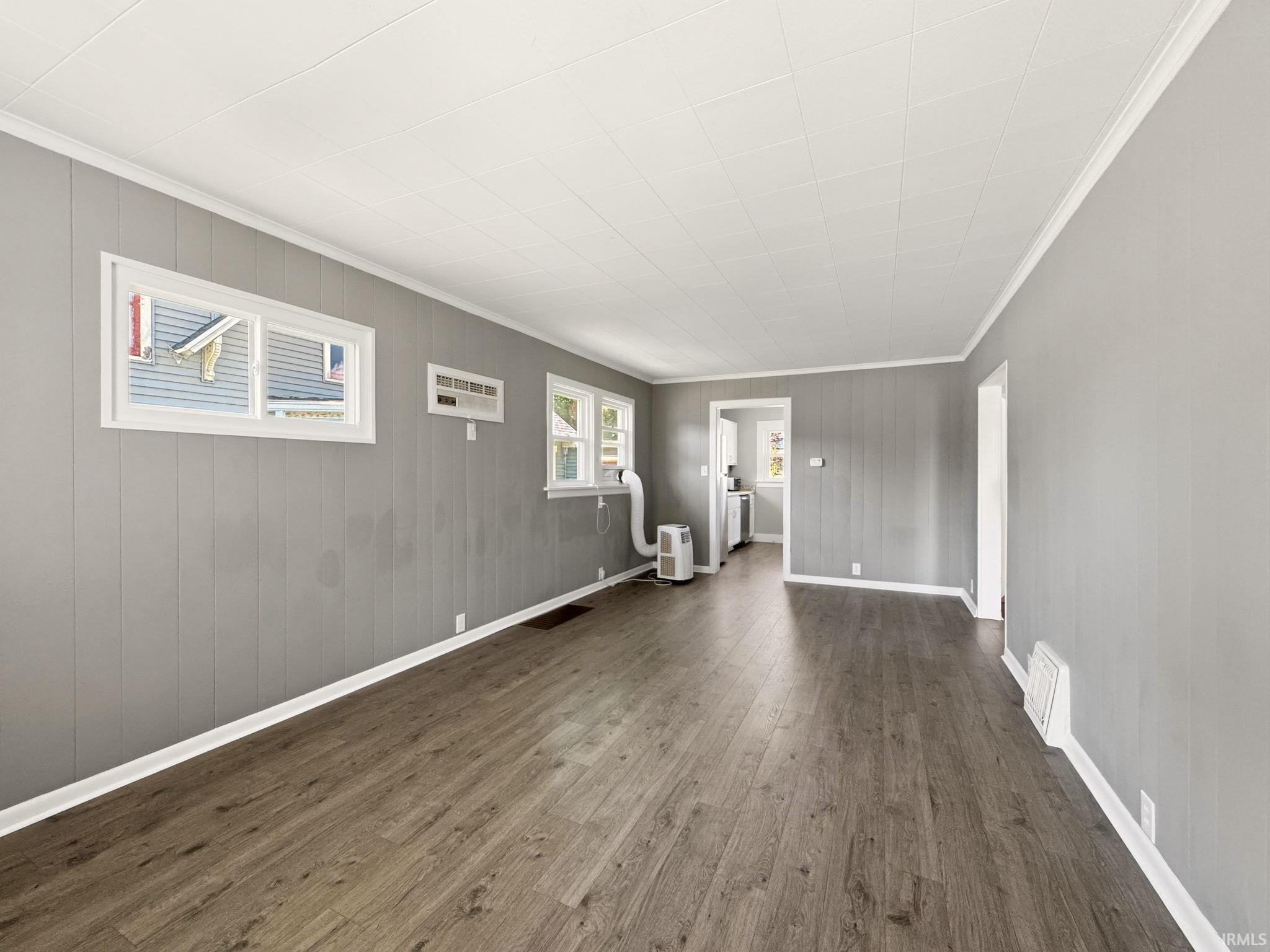 Spacious living area featuring wood-finish flooring, light gray paneling, white trim, and multiple windows