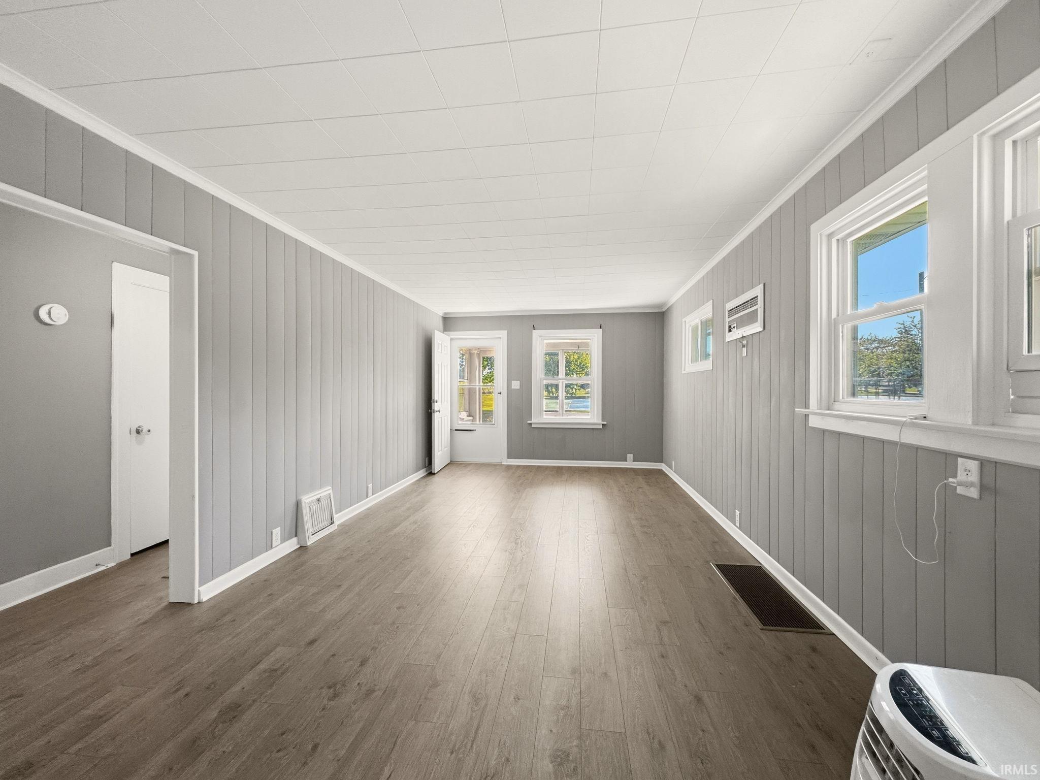 Spacious interior room featuring wood-finish flooring, light gray vertical paneling, white trim, and a textured white ceiling