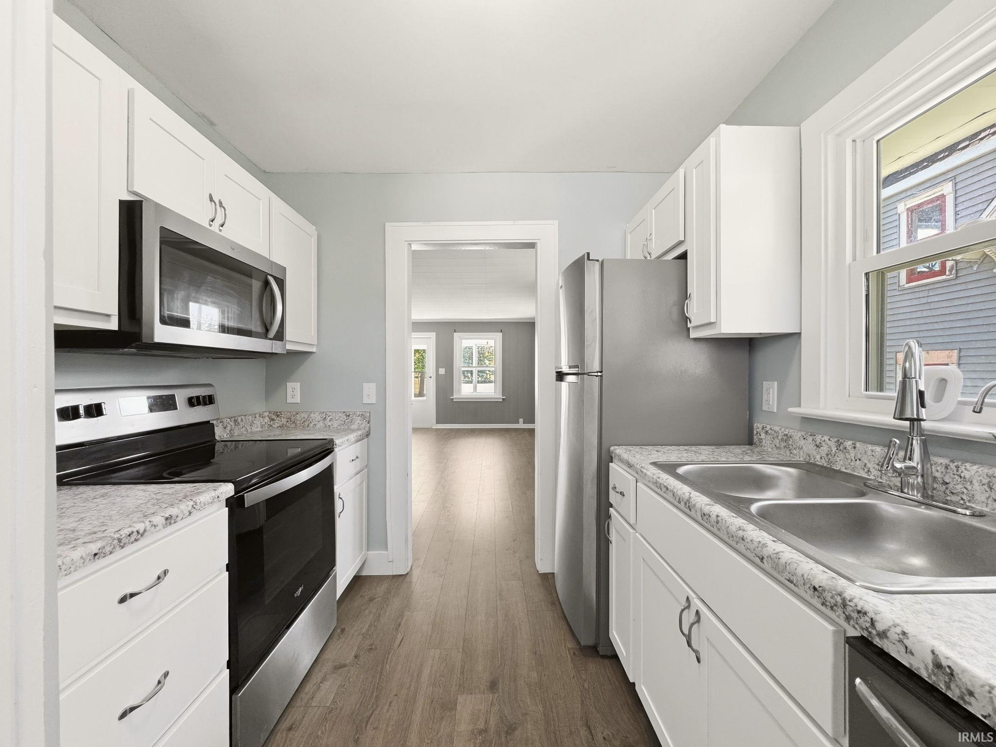 Galley kitchen featuring white cabinetry, light countertops, stainless steel appliances, and wood-finish flooring