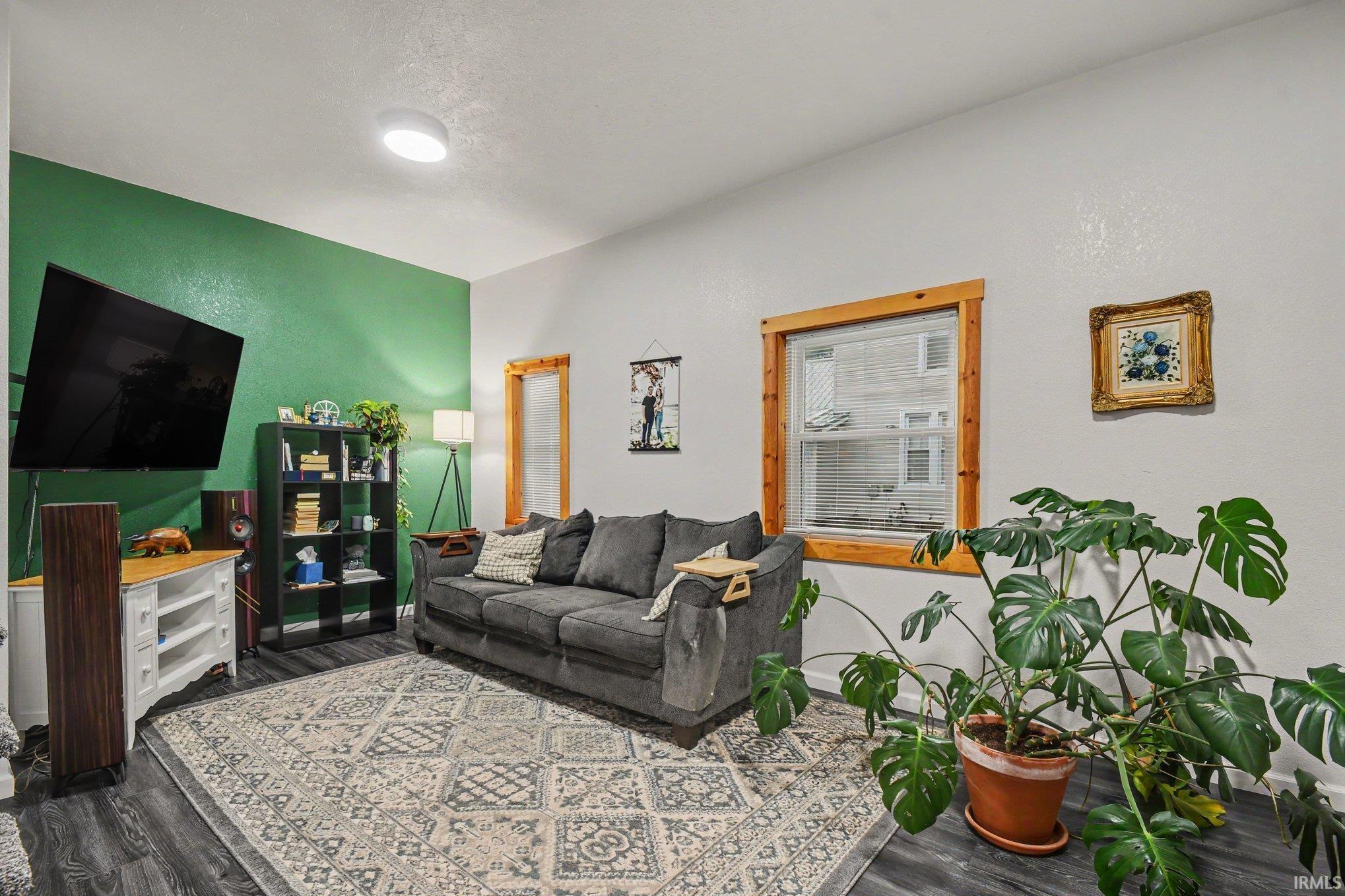 Living area featuring a distinctive green accent wall, wood-finish flooring, and a large window with natural wood trim