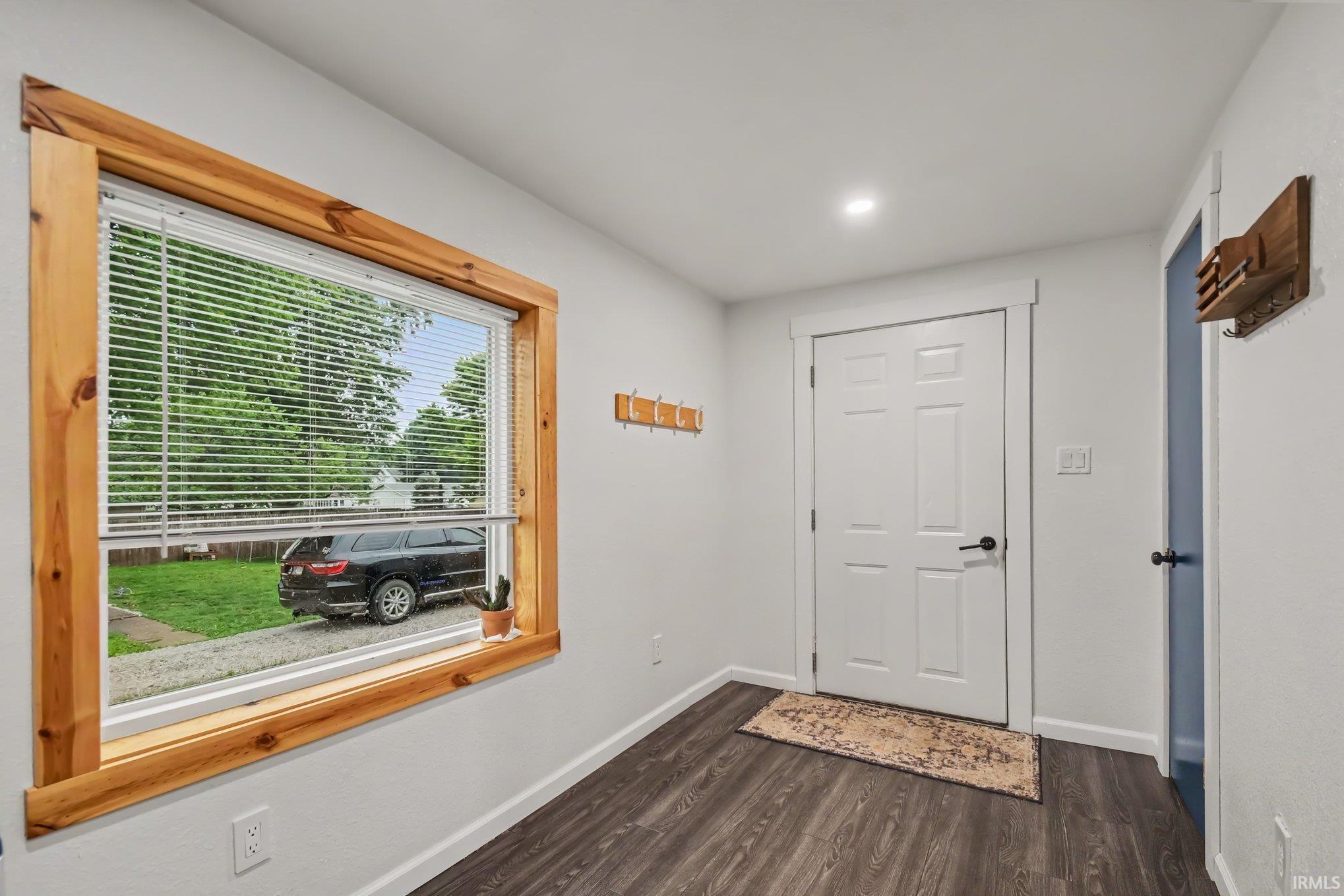 Entryway featuring wood-finish flooring, a white paneled door with black hardware, and recessed lighting