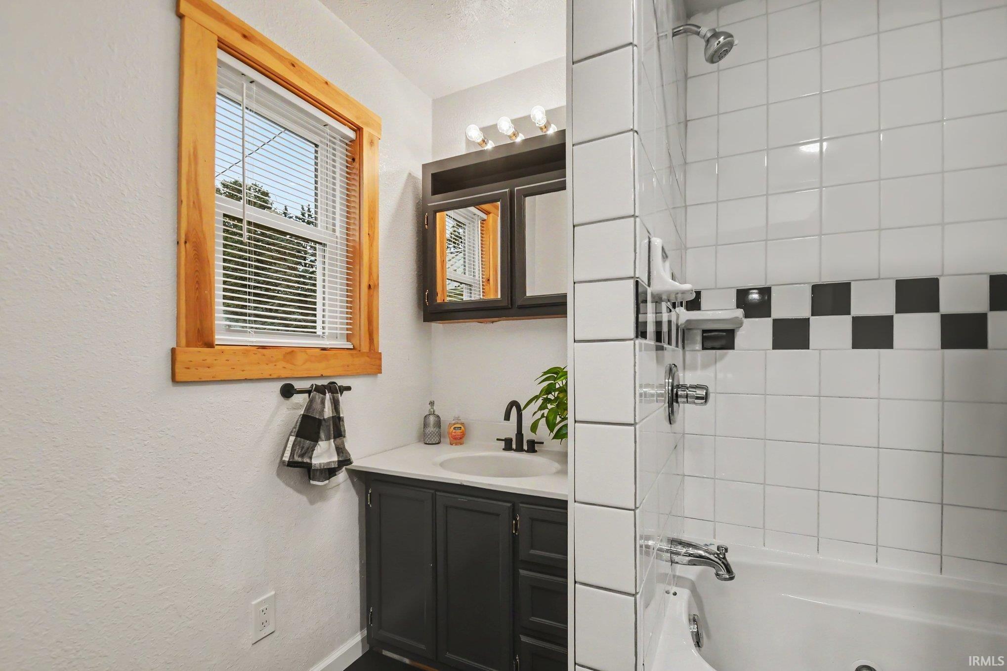 Bathroom featuring a white subway tile surround with a checkerboard accent, a built-in bathtub, and a dark wood vanity with a white countertop