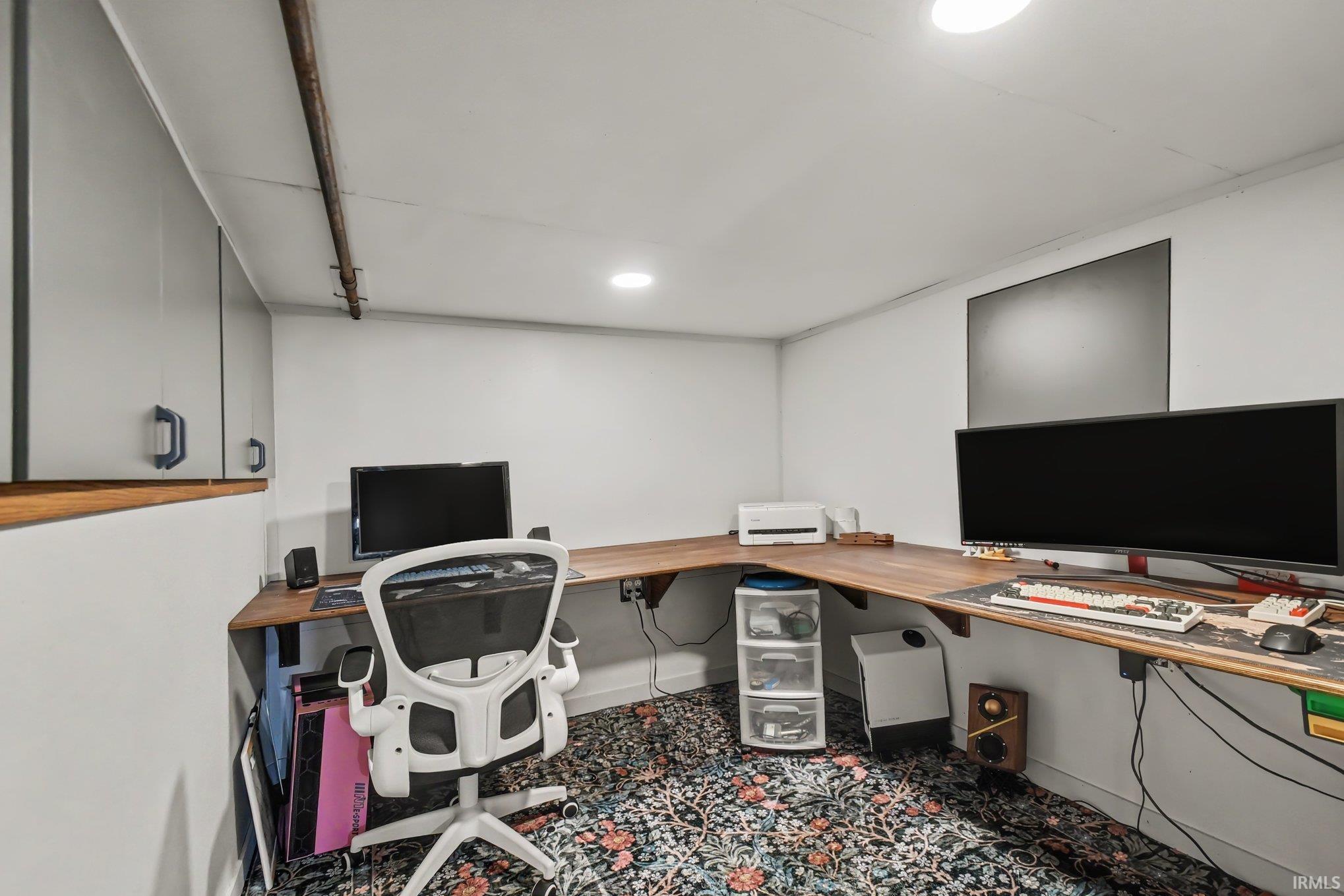 Dedicated workspace featuring wood-finish countertops, overhead built-in cabinetry, recessed lighting, and patterned carpeting