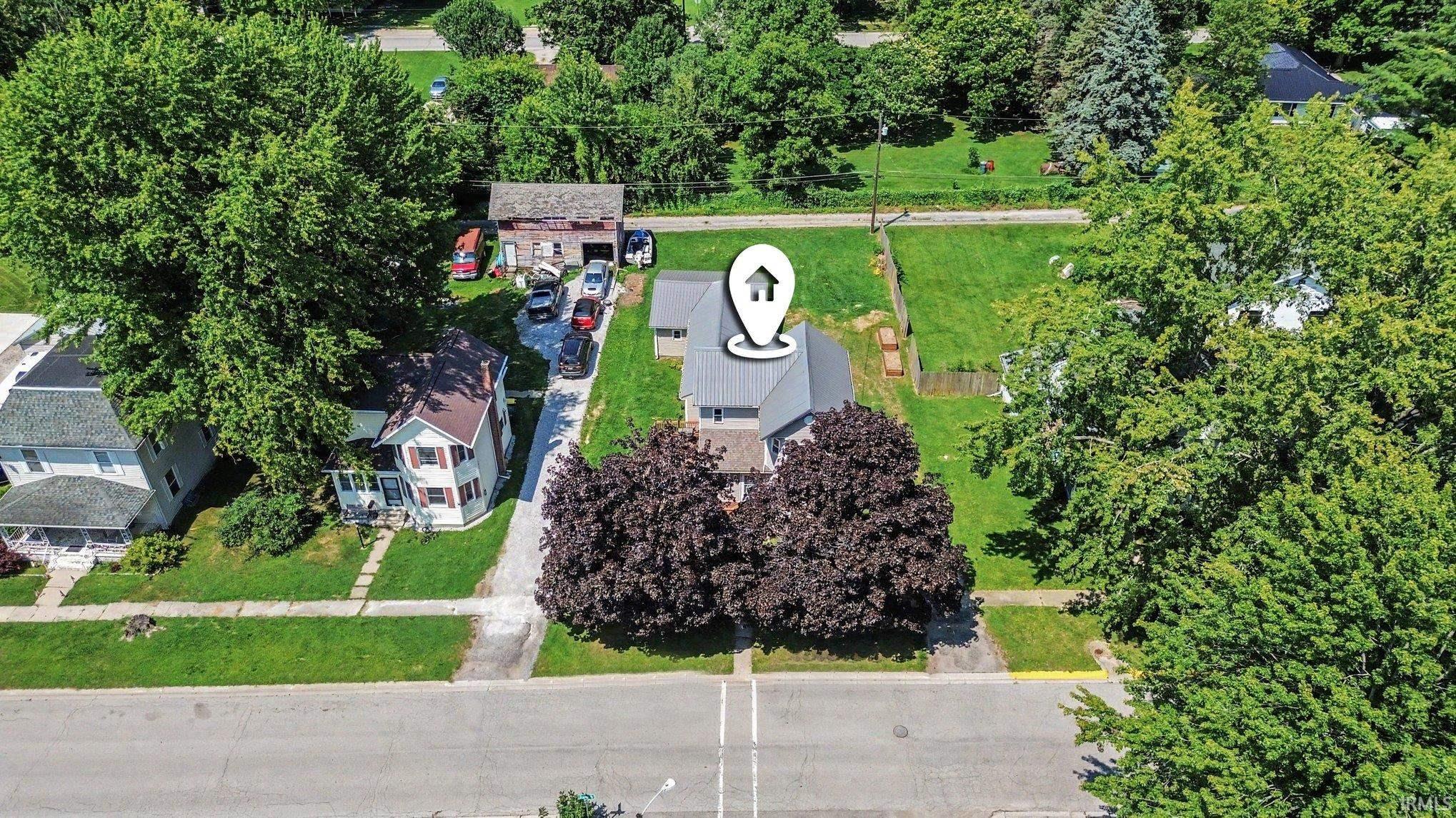 Aerial perspective showcasing a property with a gray-roofed house, a gravel driveway, a detached garage, and a large grassy yard