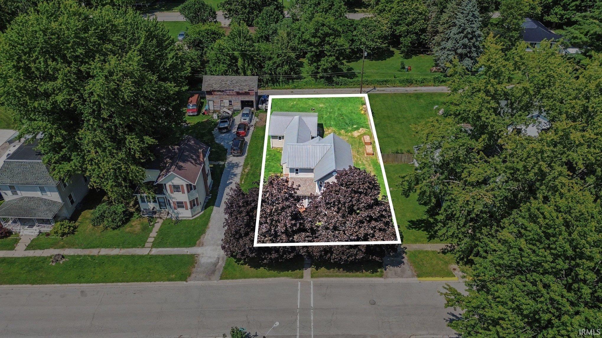 Aerial property overview highlighting a metal-roofed structure with a light-colored exterior, surrounded by mature trees