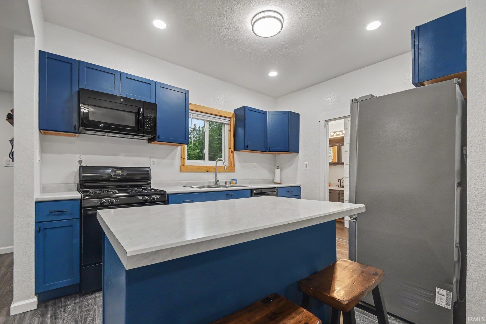 Kitchen featuring blue cabinetry, white countertops, black appliances, and a central island