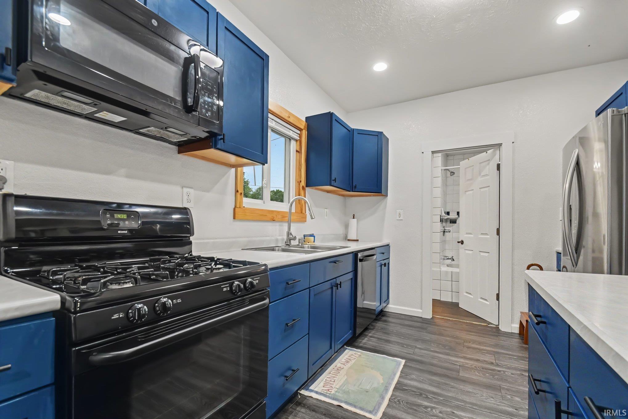 Kitchen with blue shaker-style cabinetry, light countertops, and dark wood-finish flooring