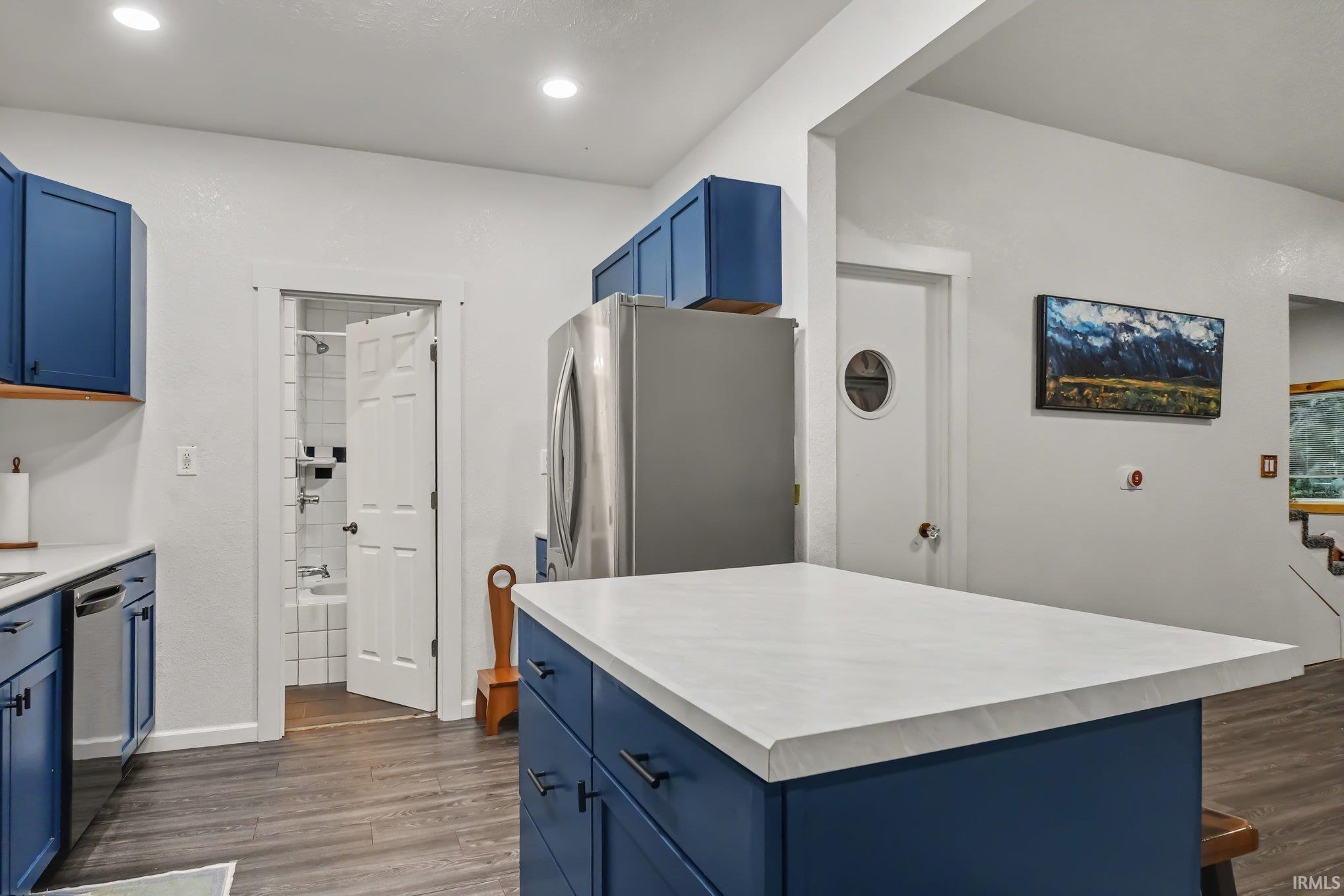 Kitchen featuring blue cabinetry, a central island with a light-toned countertop, stainless steel appliances, and wood-finish flooring