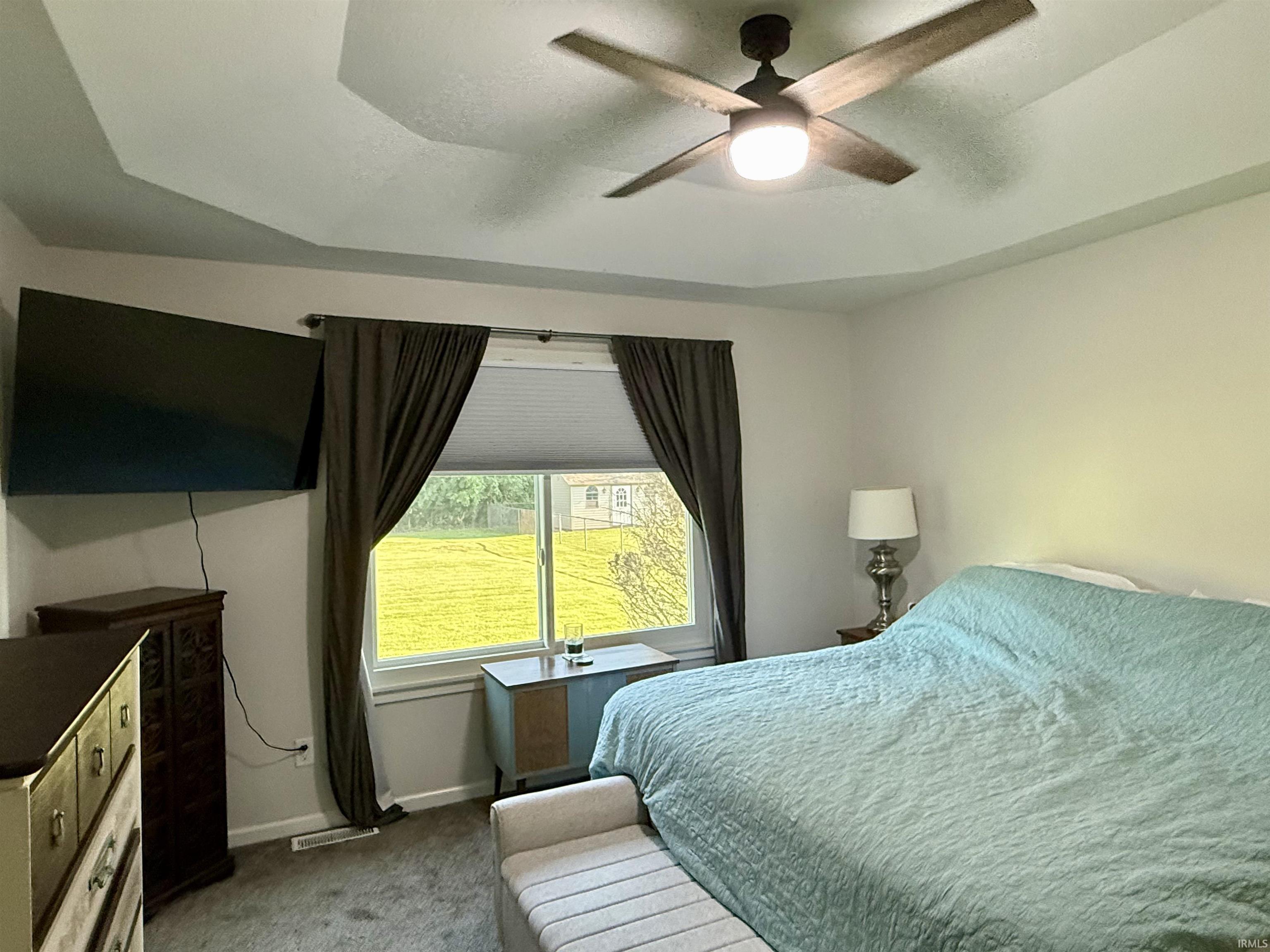 Bright secondary bedroom featuring expansive glass sliding doors with operable windows, dark curtain panels, ceiling fan with integrated lighting, carpet flooring, and built-in dresser with mirror