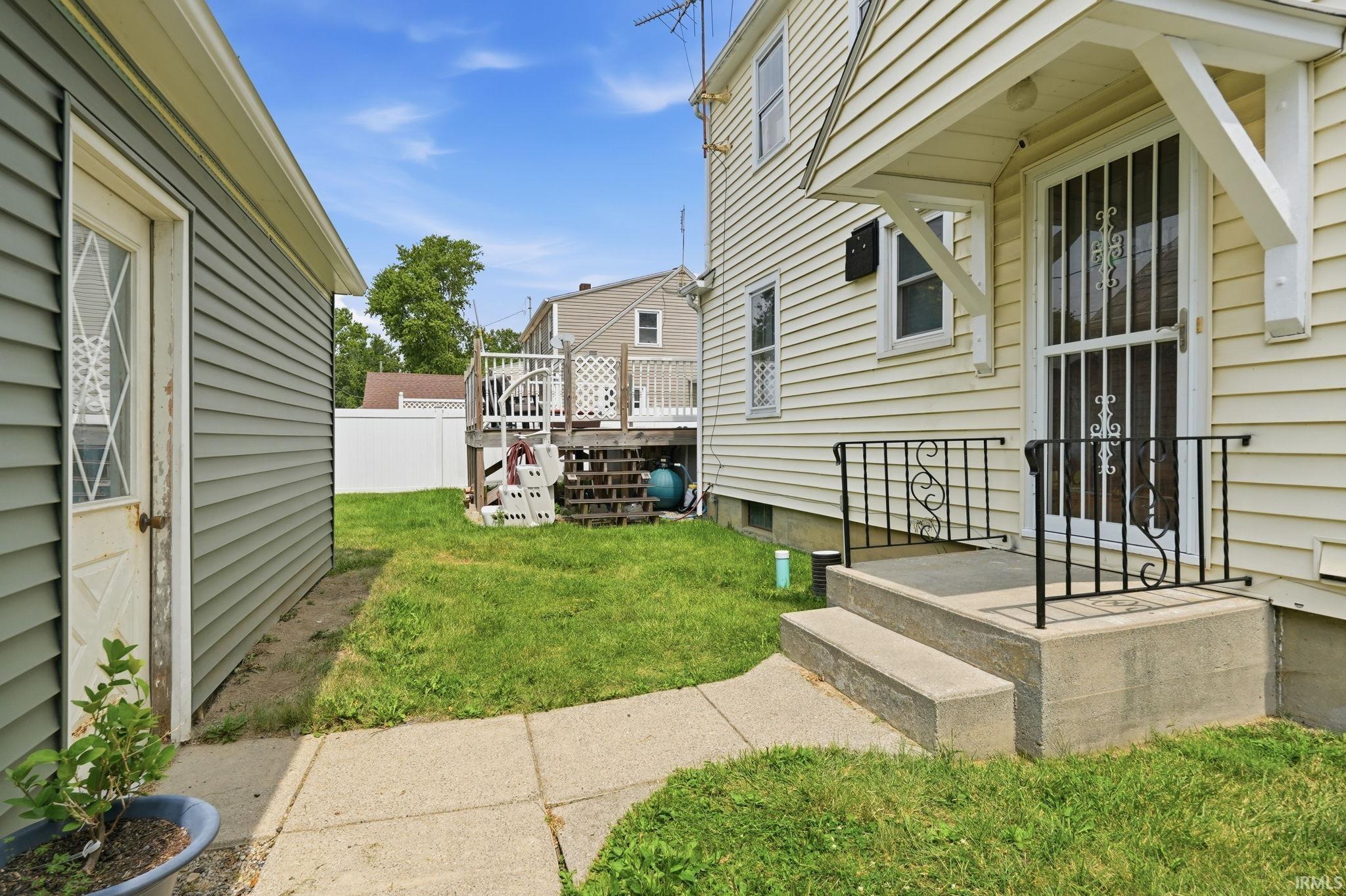 Rear exterior featuring a concrete walkway, two-tier deck, privacy fencing, and a detached structure with siding