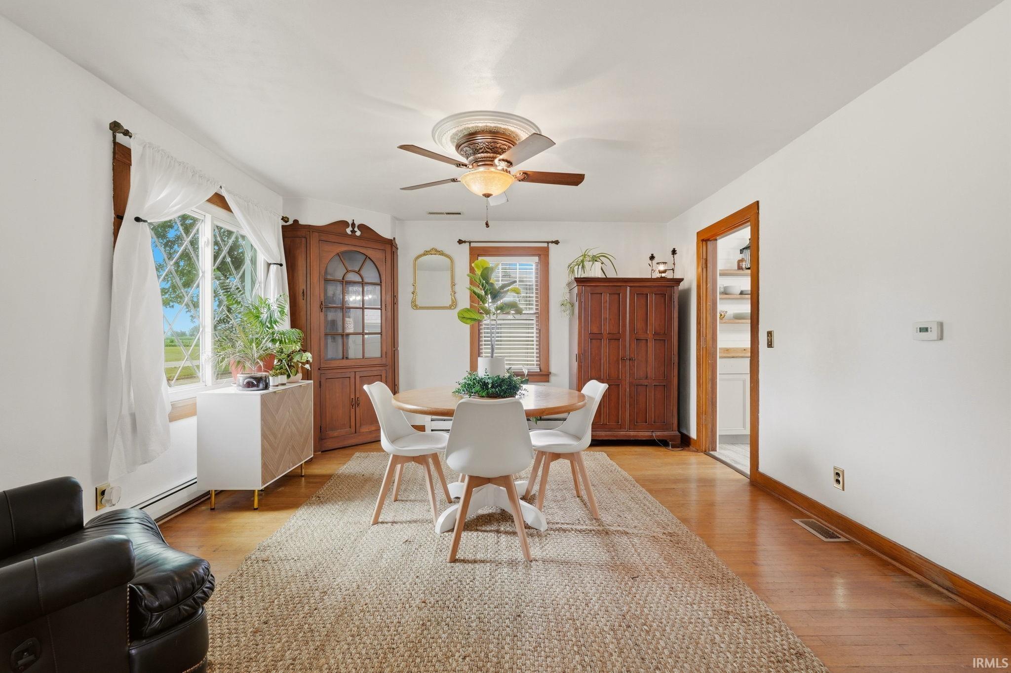 Bright interior space featuring wood-finish flooring, a decorative corner cabinet with glass paned doors, and a ceiling fan with integrated lighting