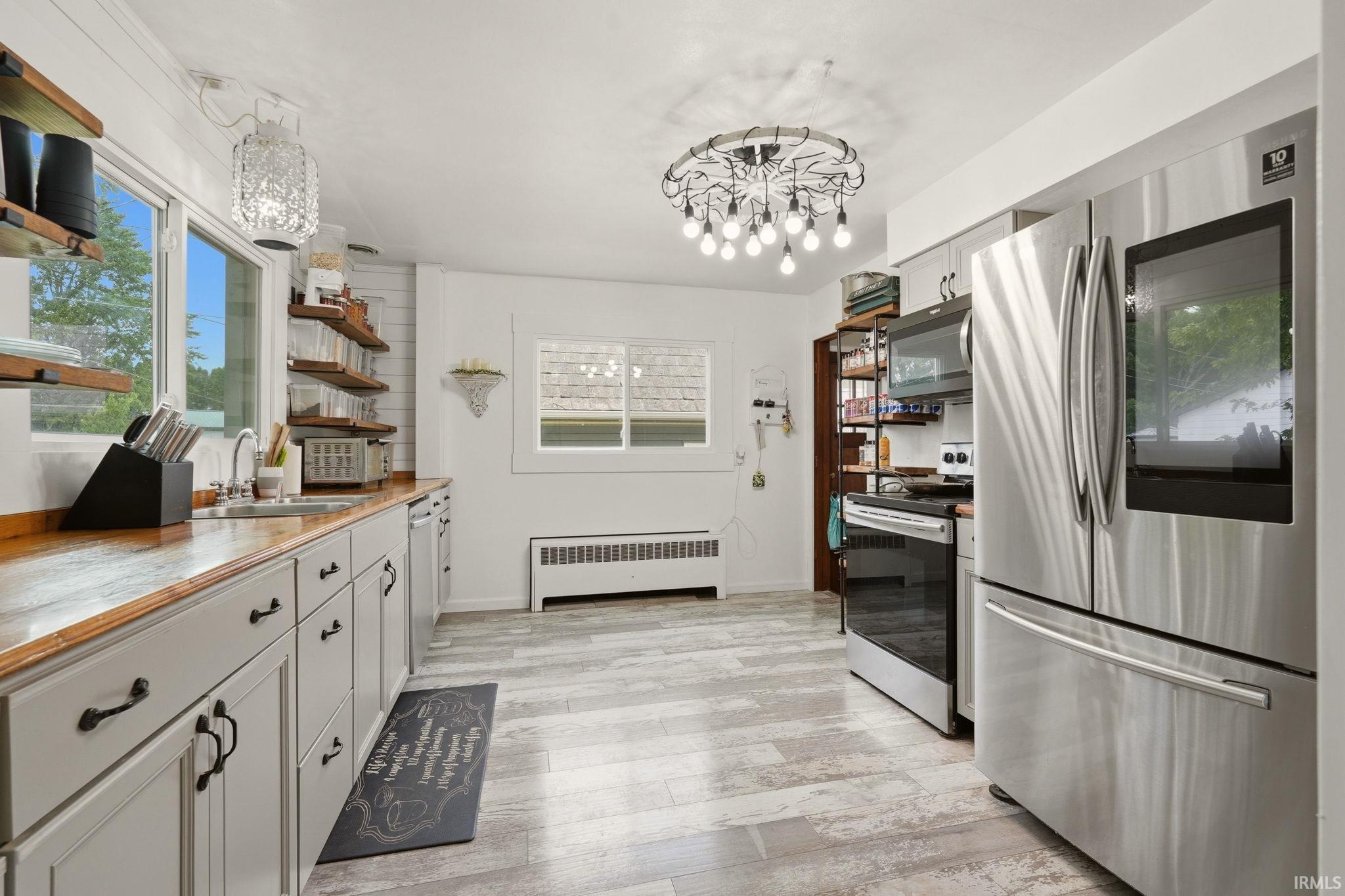 Bright kitchen featuring wood-finish countertops, stainless steel appliances, and light grey base cabinetry with black hardware