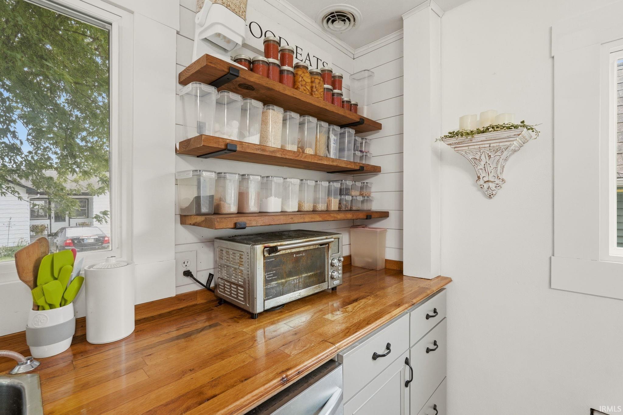 Kitchen features include a wood-finish countertop, crisp white cabinetry with dark hardware, and open wood shelving against a shiplap accent wall
