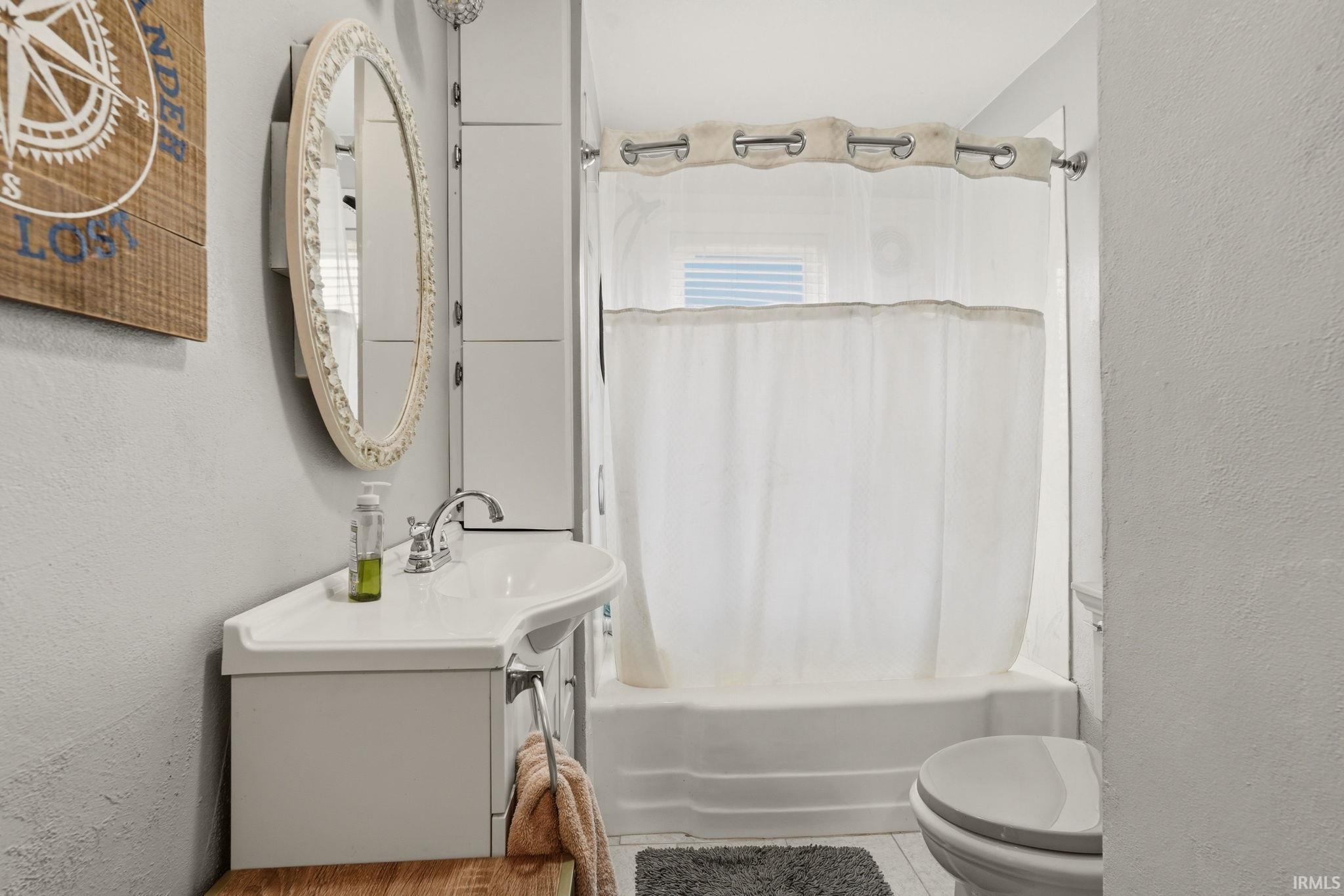 Bathroom featuring a white corner sink vanity, polished chrome faucet, oval mirror, and a white tub/shower combination with a shower curtain rod
