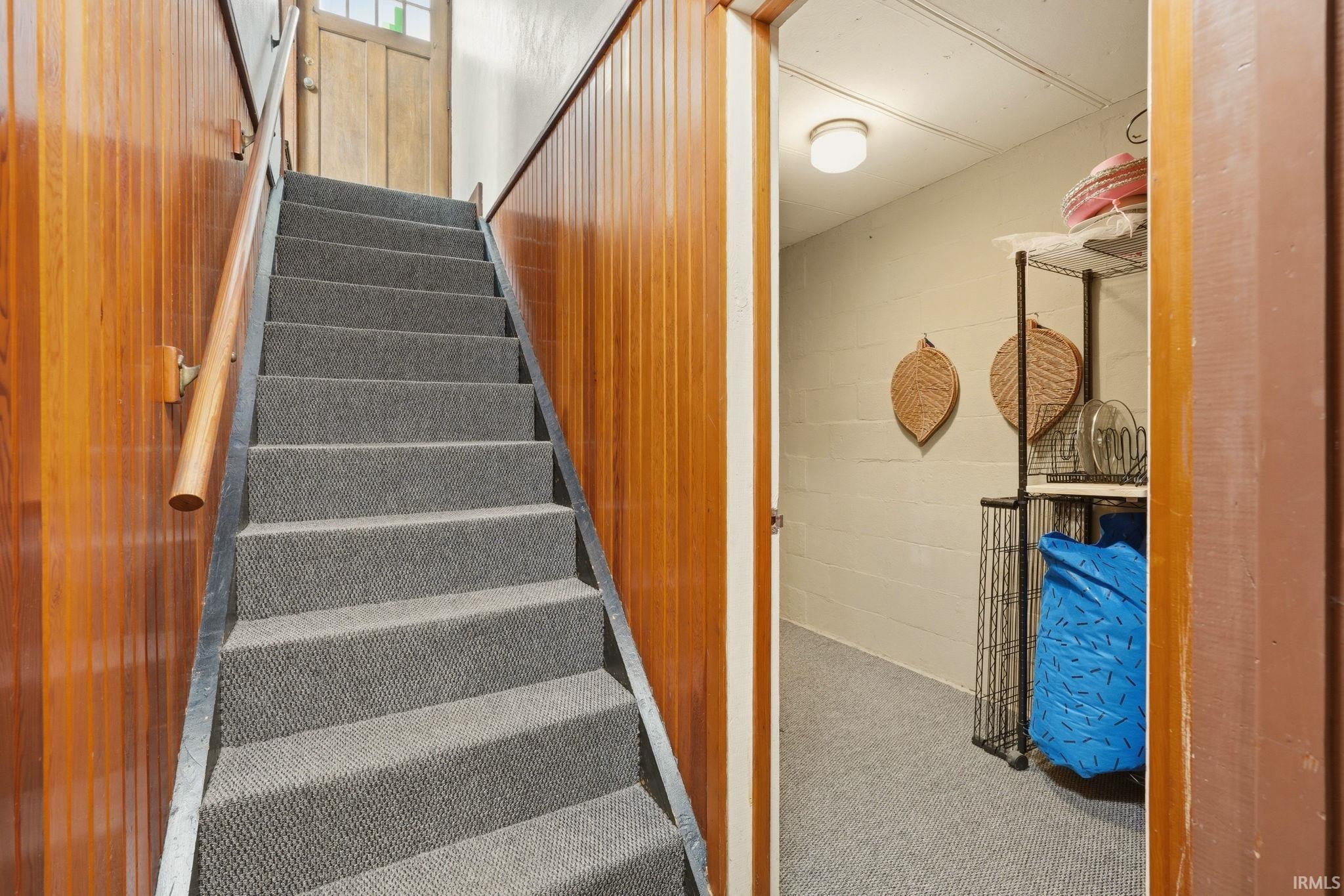 Practical basement staircase with charcoal-gray carpeted treads and wooden handrails, flanked by finished wood-paneled walls