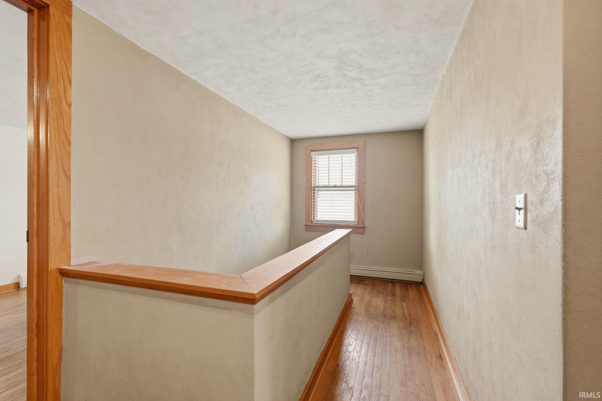 Hallway featuring wood-finish flooring, a wood balustrade, and a window with blinds