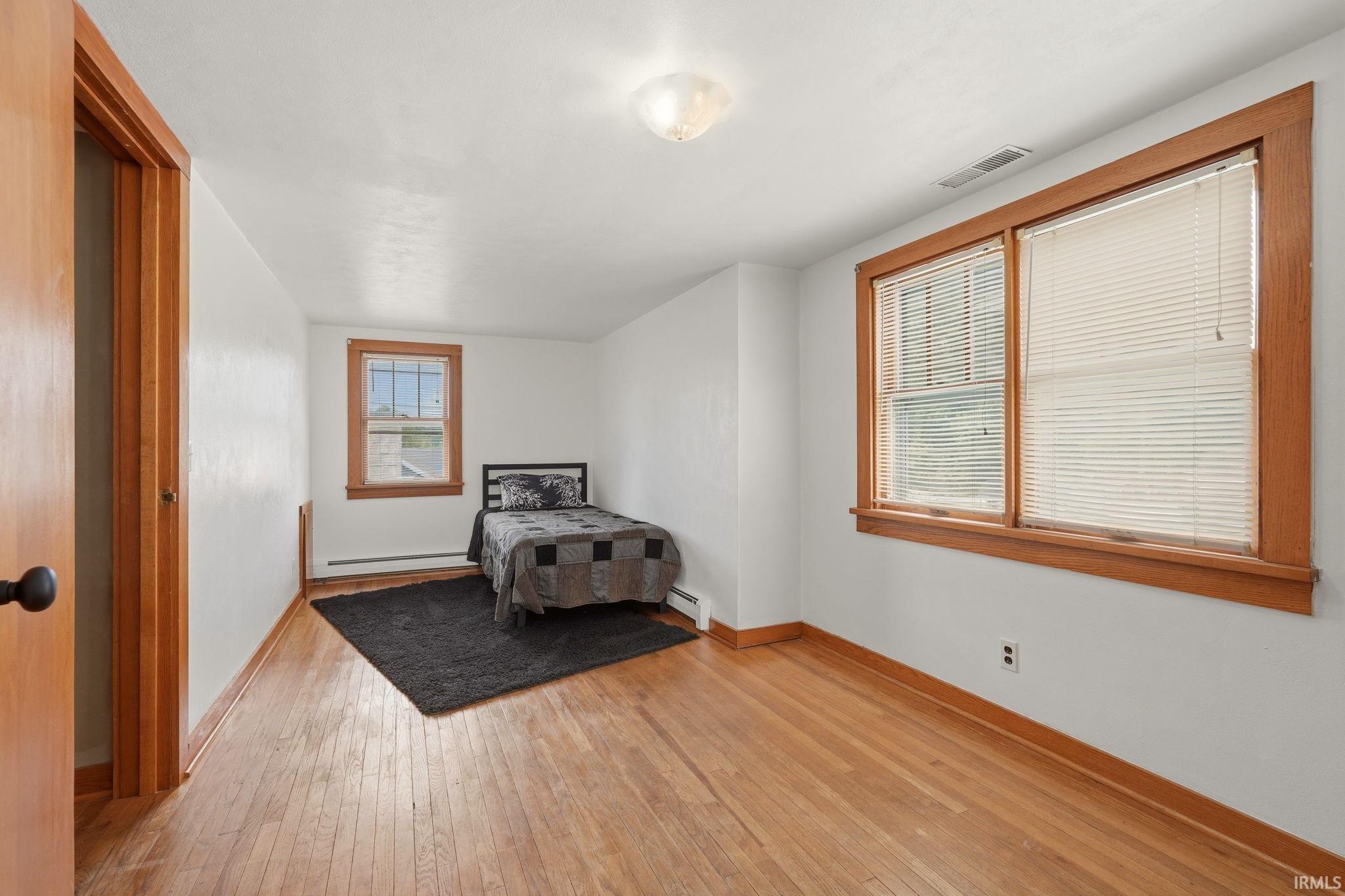 Hardwood flooring extending throughout, white walls, and wood trim around windows and door frame