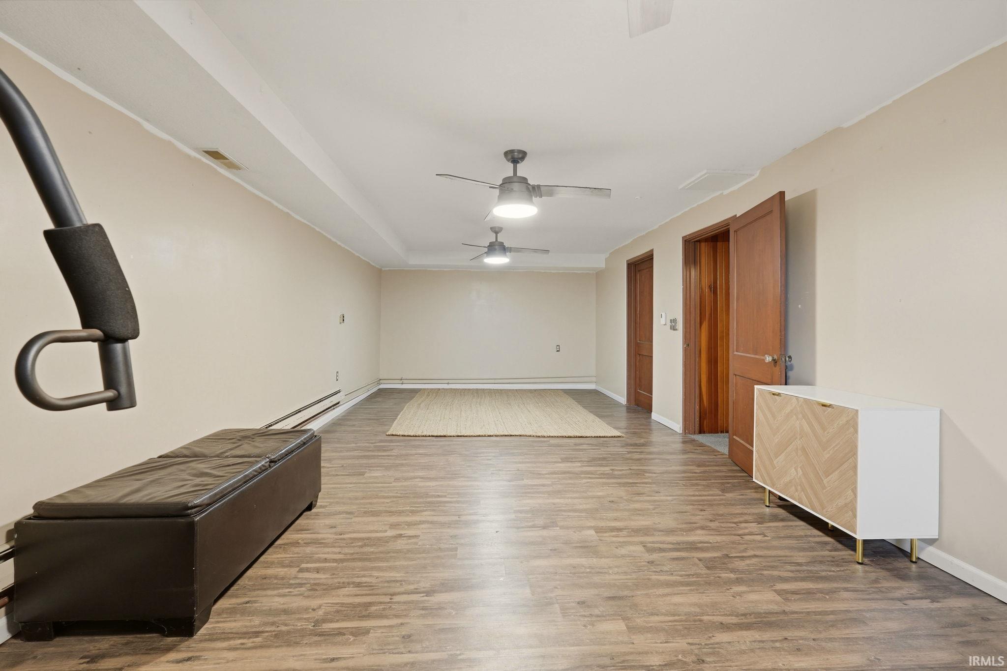 Spacious room featuring wood-finish flooring, light-toned walls, and multiple ceiling fans