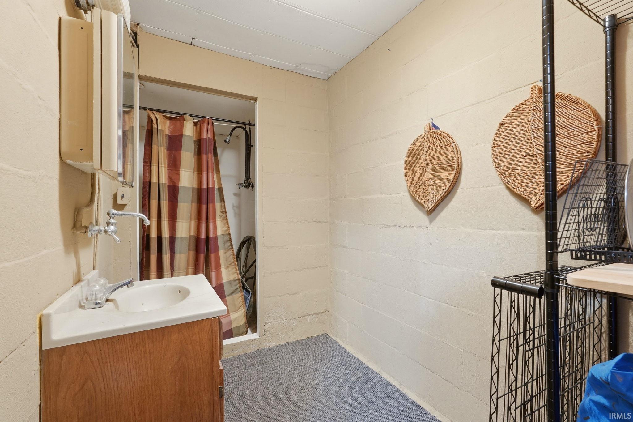 Compact bathroom featuring a corner vanity with integrated sink, chrome faucet, and a shower with a plaid curtain
