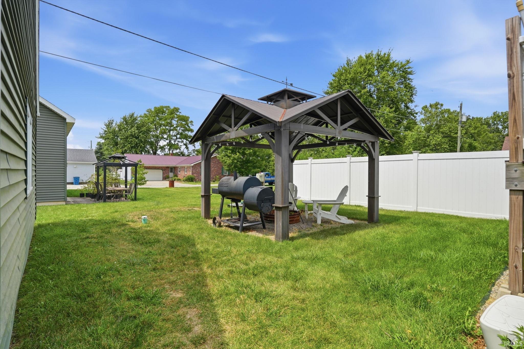 Grassed yard area featuring a built-in gazebo with a metal roof and a privacy fence