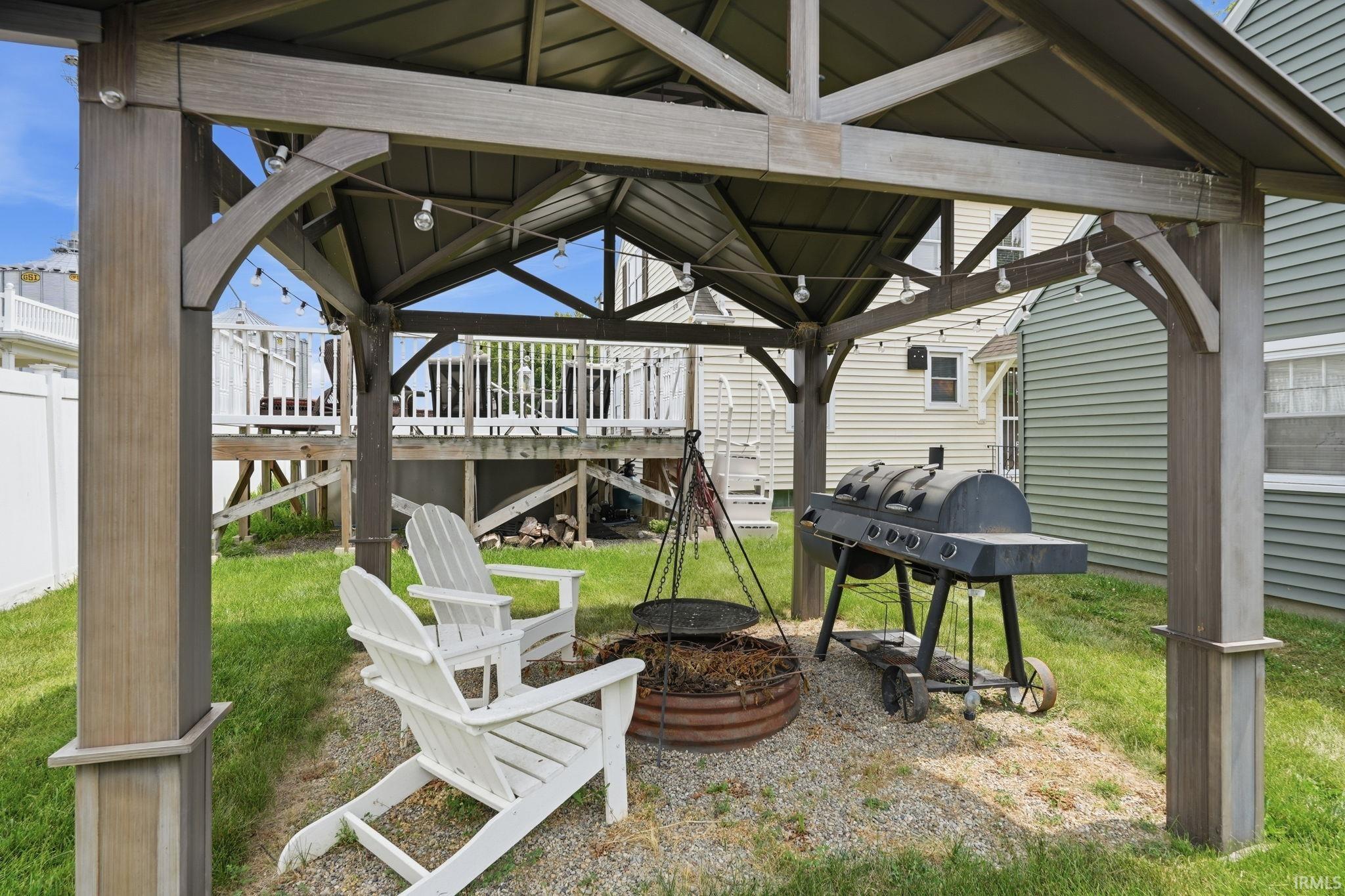 Freestanding gazebo with string lighting, gravel ground cover, and a fire pit