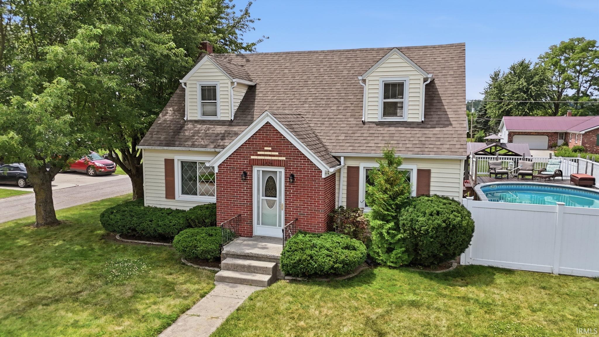 Charming two-story home featuring a brick entryway, dormer windows, and an above-ground pool