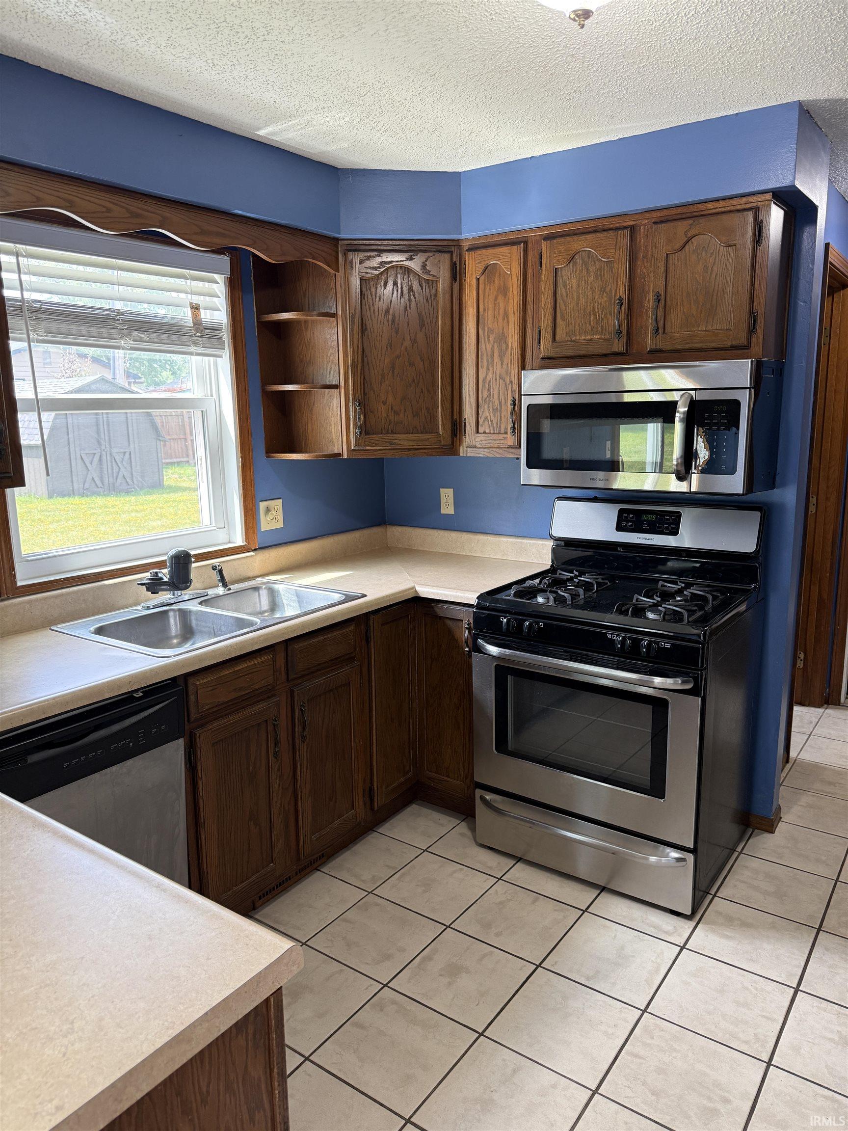 Kitchen featuring wood cabinetry, stainless steel appliances, a double basin sink, light-toned countertops, and tile flooring