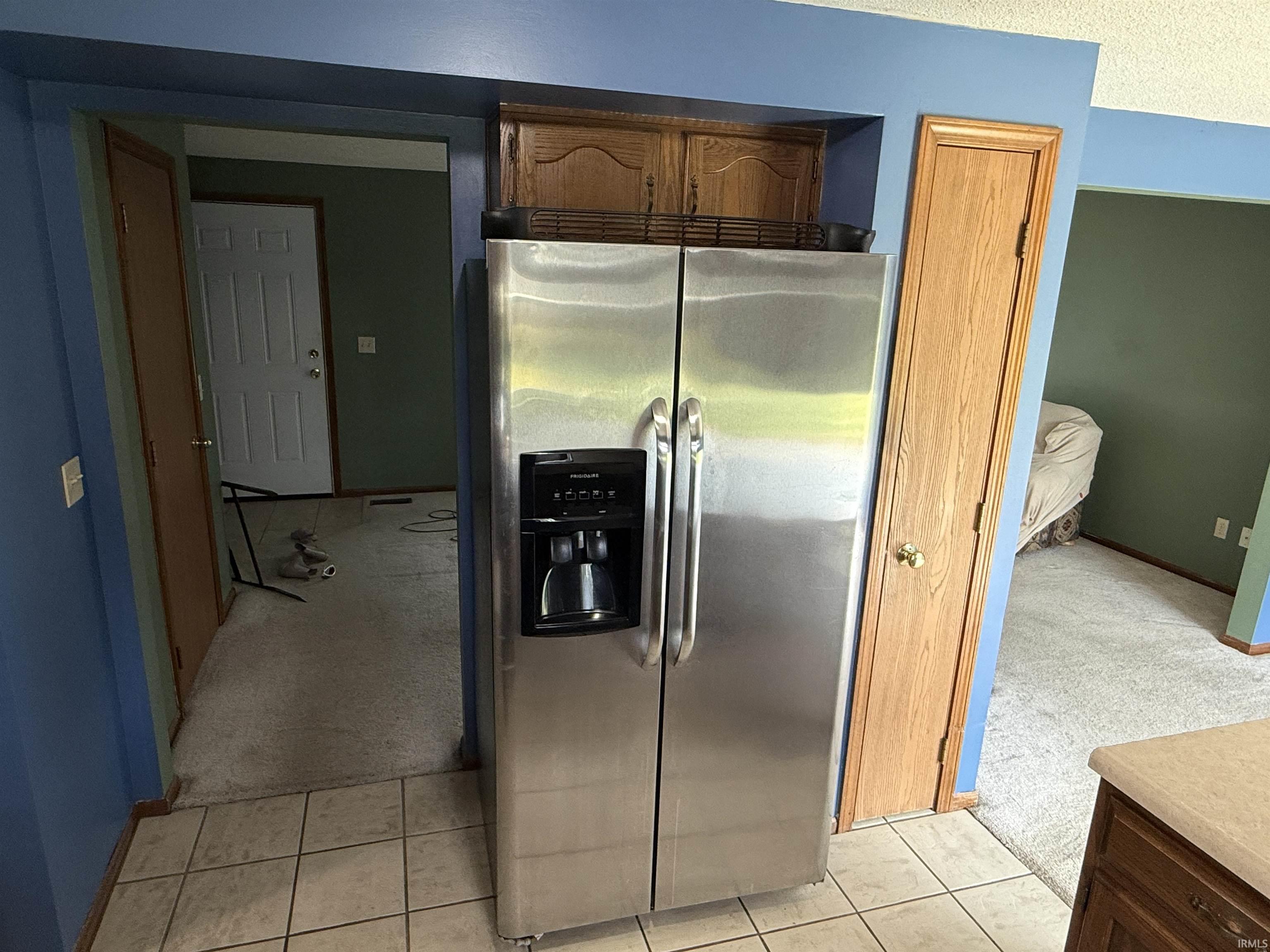 Stainless steel French-door refrigerator, integrated water and ice dispenser, tile flooring, wood cabinetry, and solid surface countertop