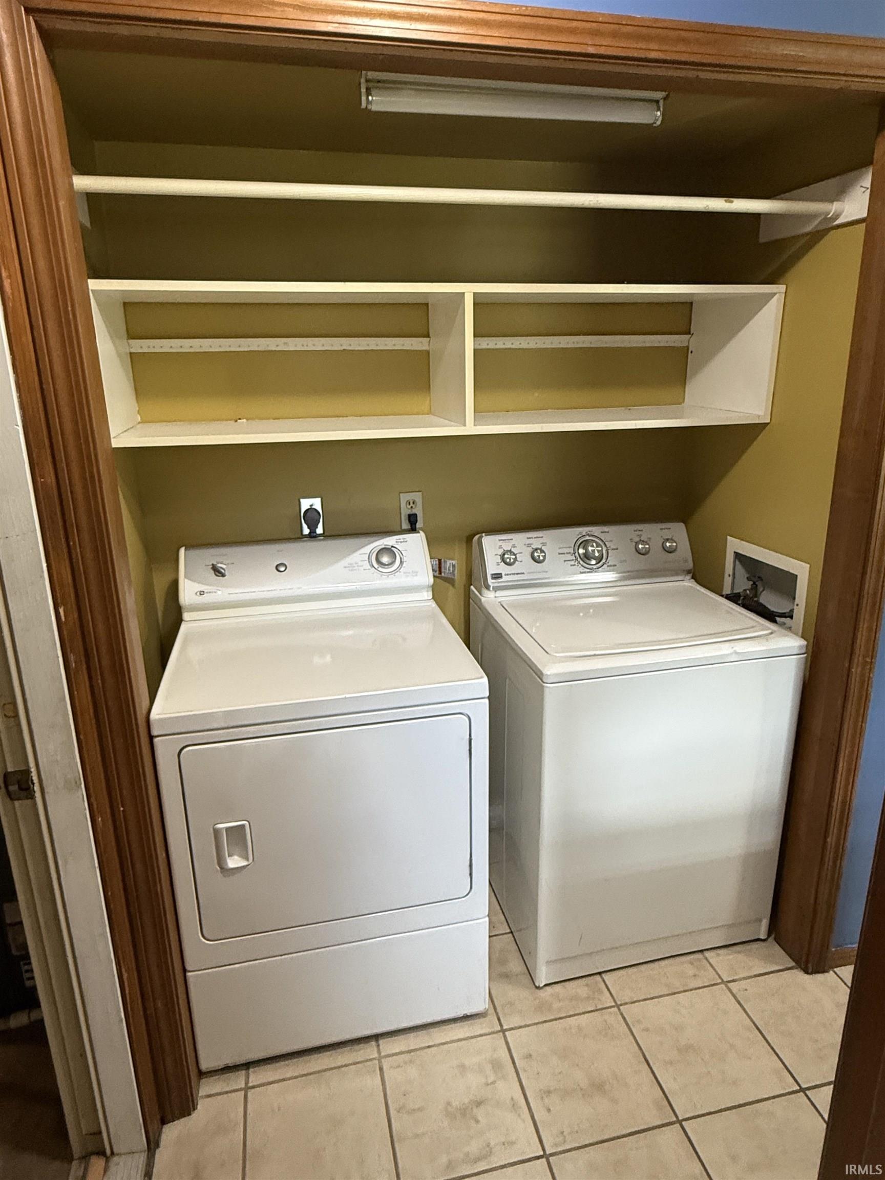 Dedicated laundry area featuring a washer and dryer, tiled flooring, built-in shelving, and an overhead hanging rod