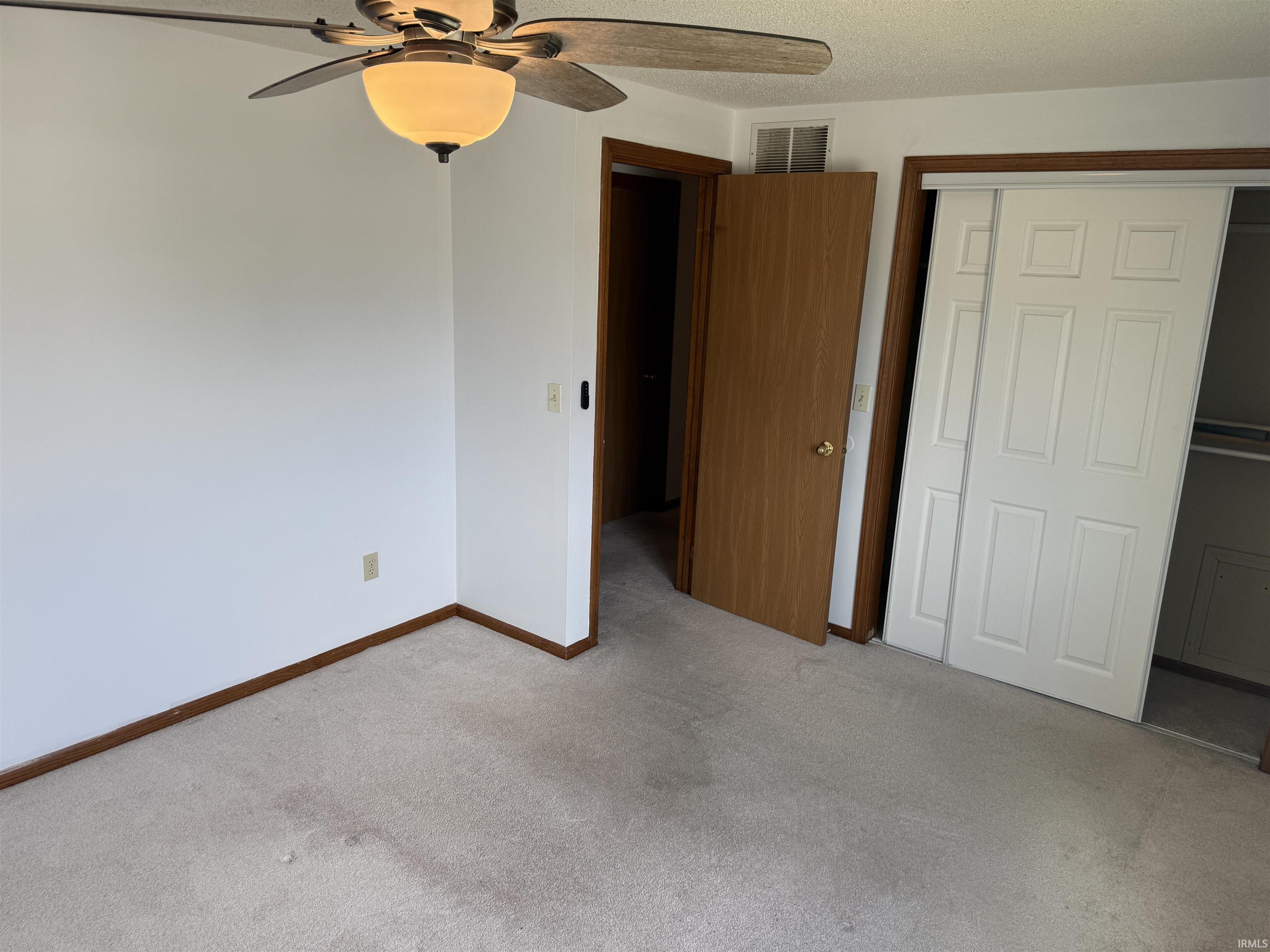 Carpeted interior space with white walls and wood-finish trim, featuring a ceiling fan with light fixture and a sliding door closet