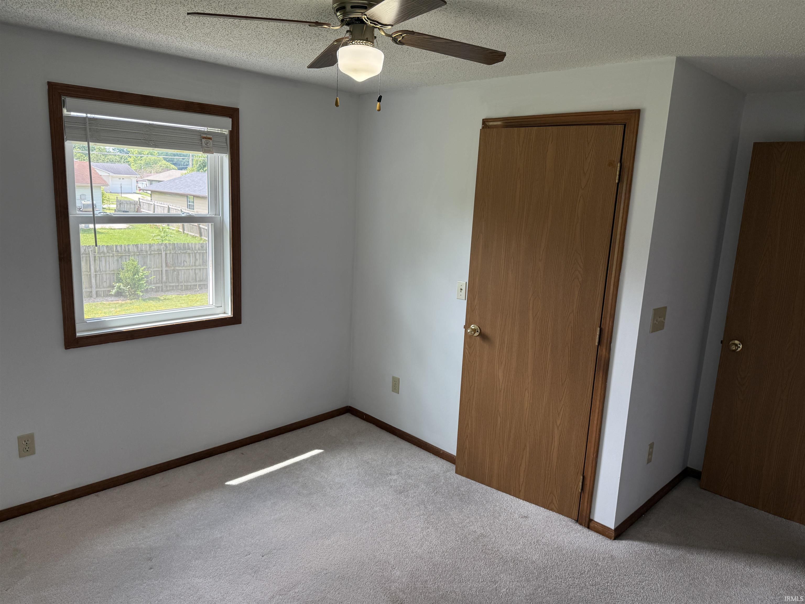 Bedroom featuring a double-hung window with a wood-stained frame, light-colored carpeting, a ceiling fan with integrated lighting, and wood-paneled doors with brass hardware