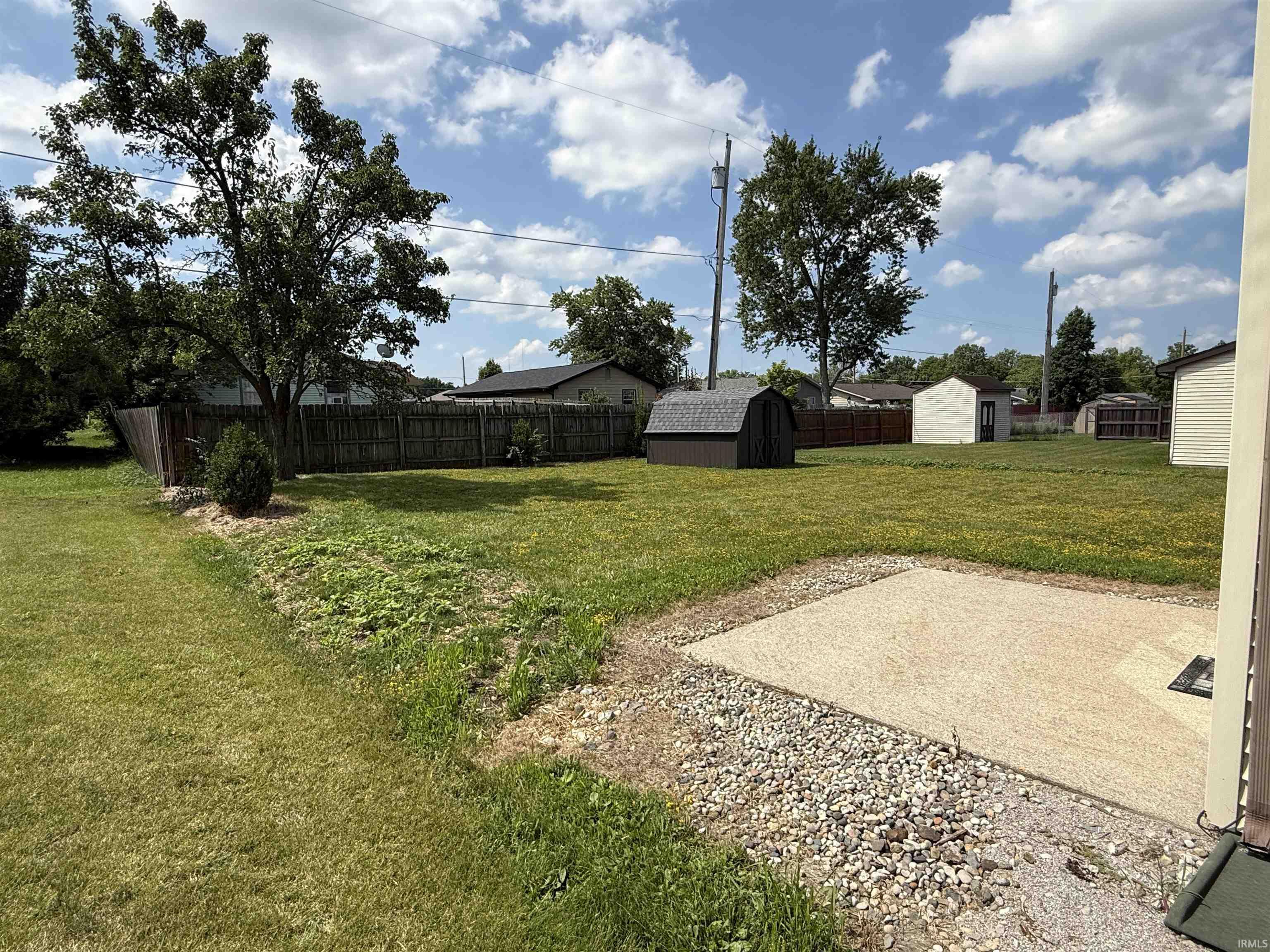 Expansive grassy yard featuring a concrete patio, a gravel border, and a privacy fence