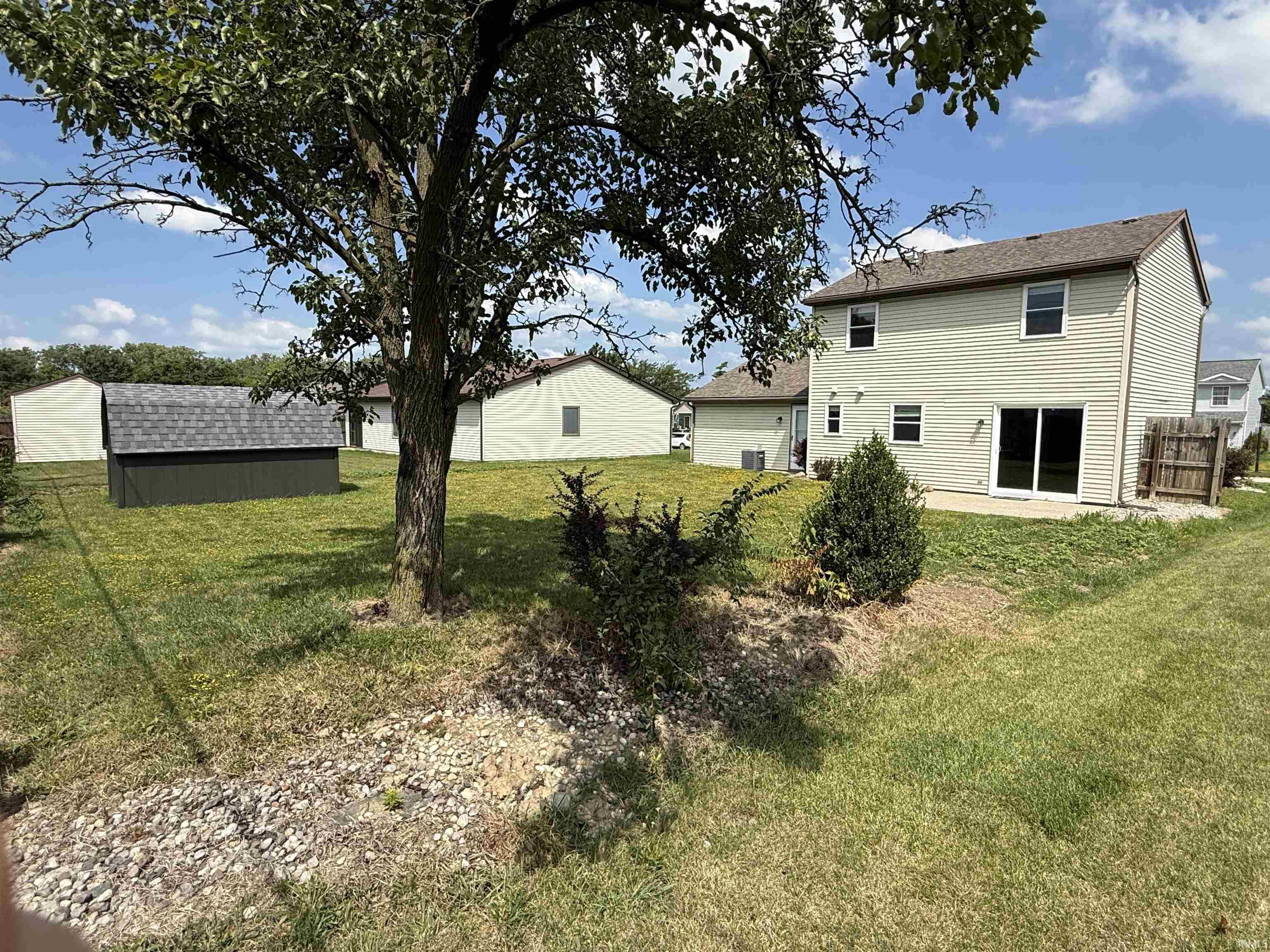 Spacious backyard featuring a two-story residence with light-colored siding, a sliding glass patio door, and a concrete patio area