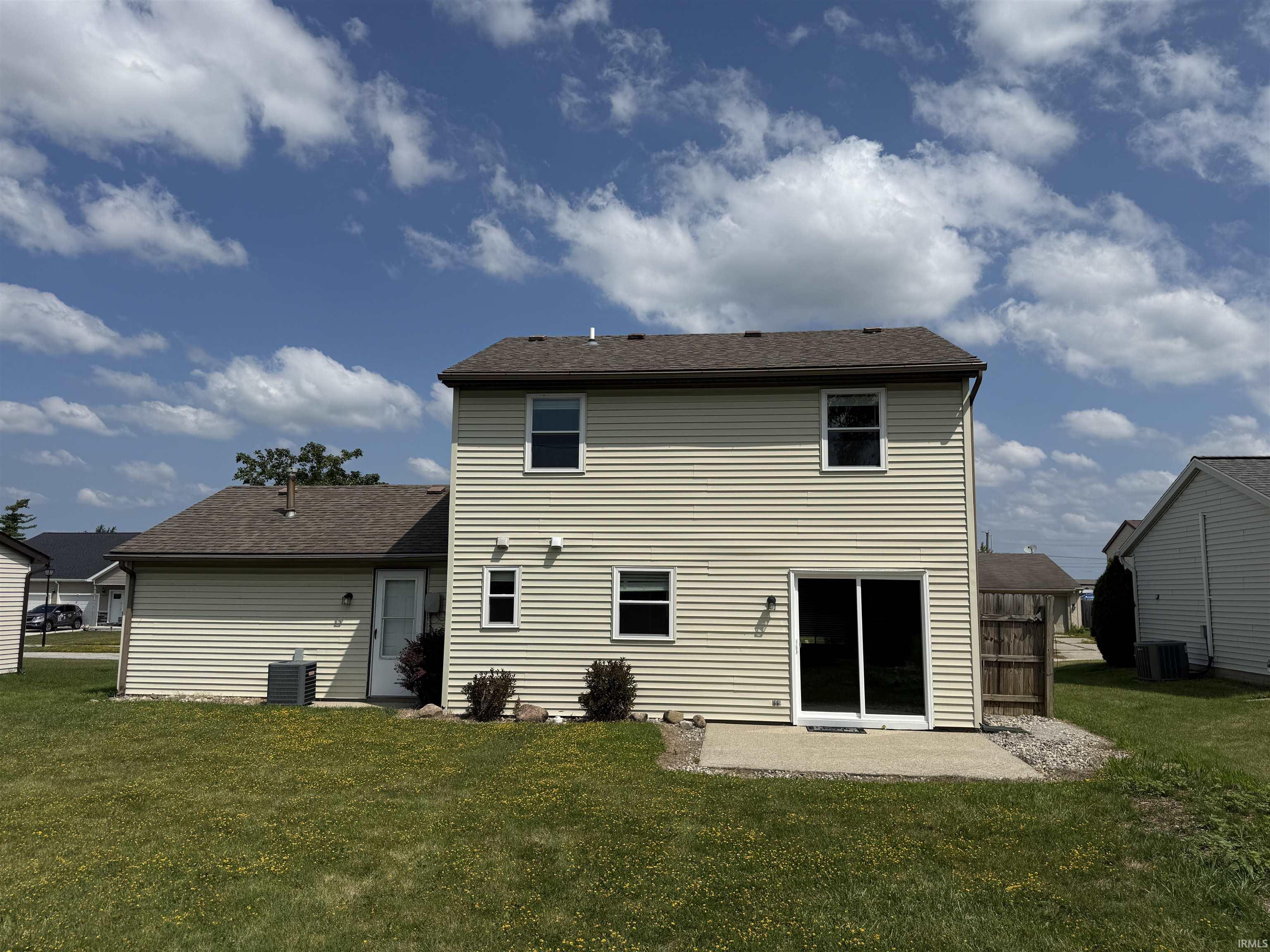 Rear exterior featuring a two-story structure with tan siding and a brown shingle roof