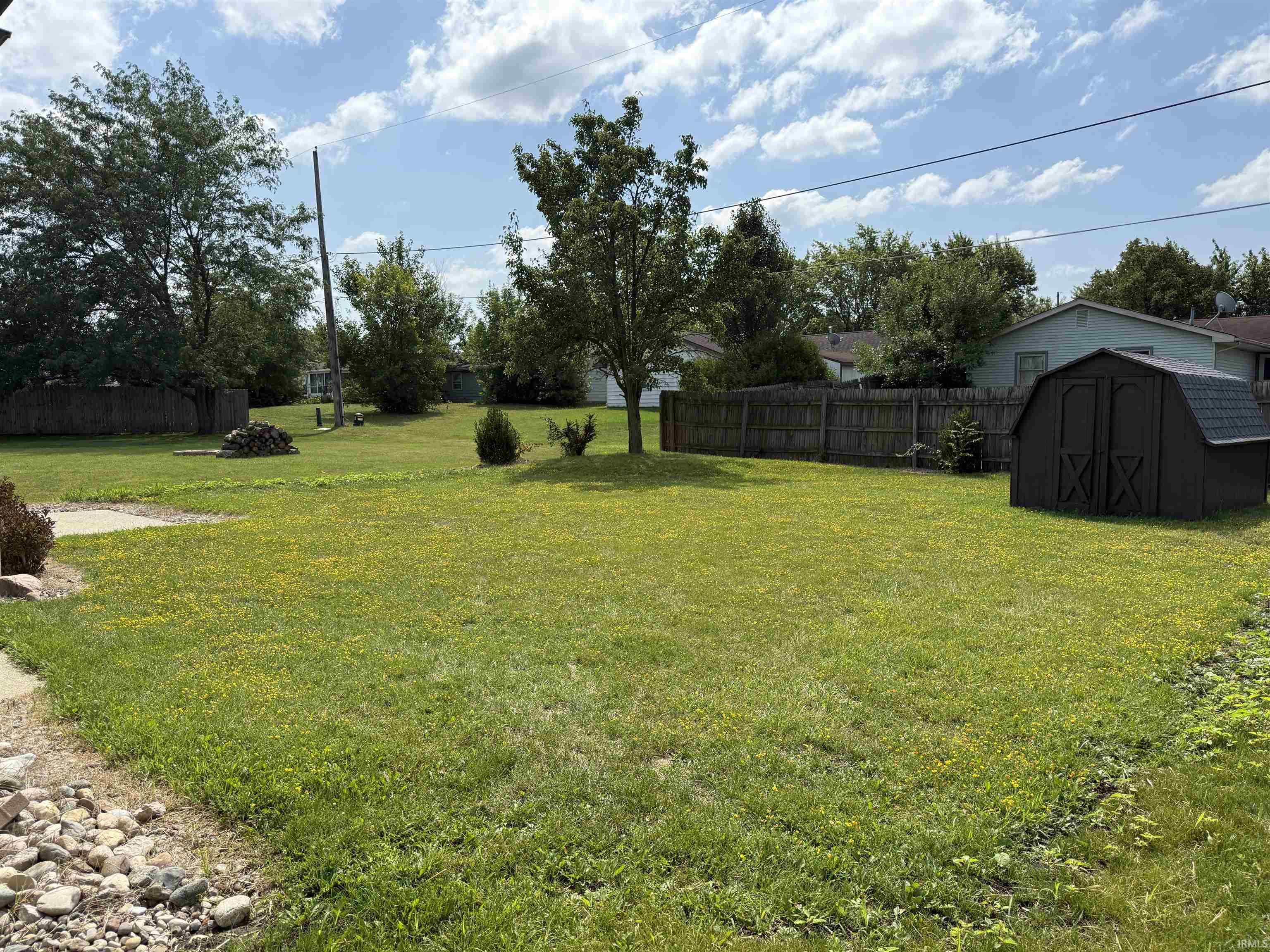 Spacious green lawn featuring a privacy fence, mature trees, and a dark brown storage shed with a shingled roof