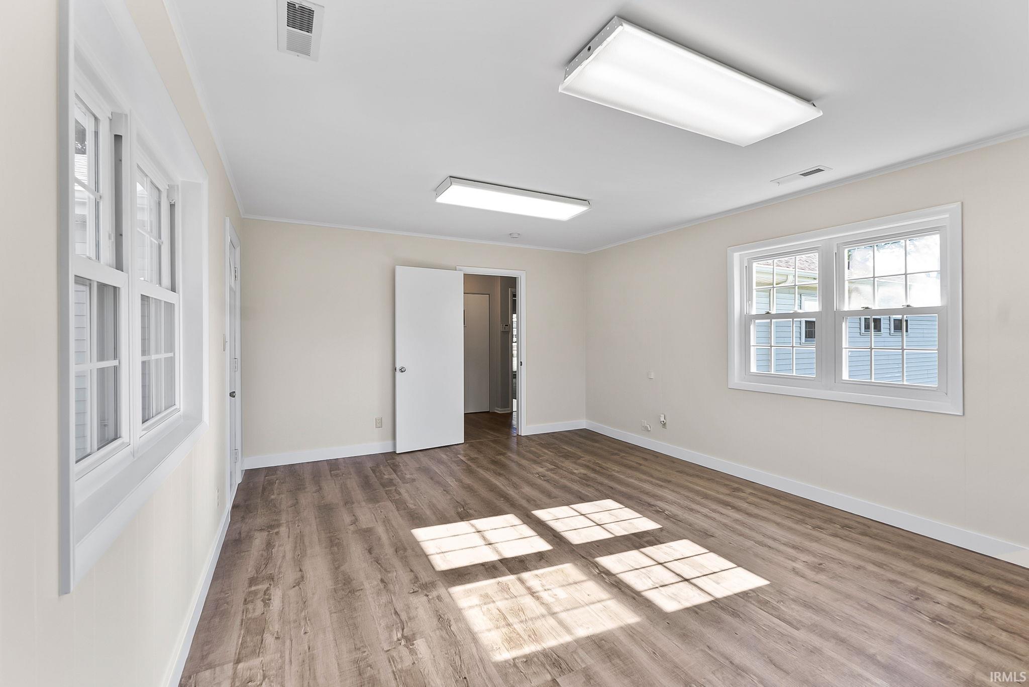 Spacious interior room with wood-finish flooring, multiple windows, and recessed lighting