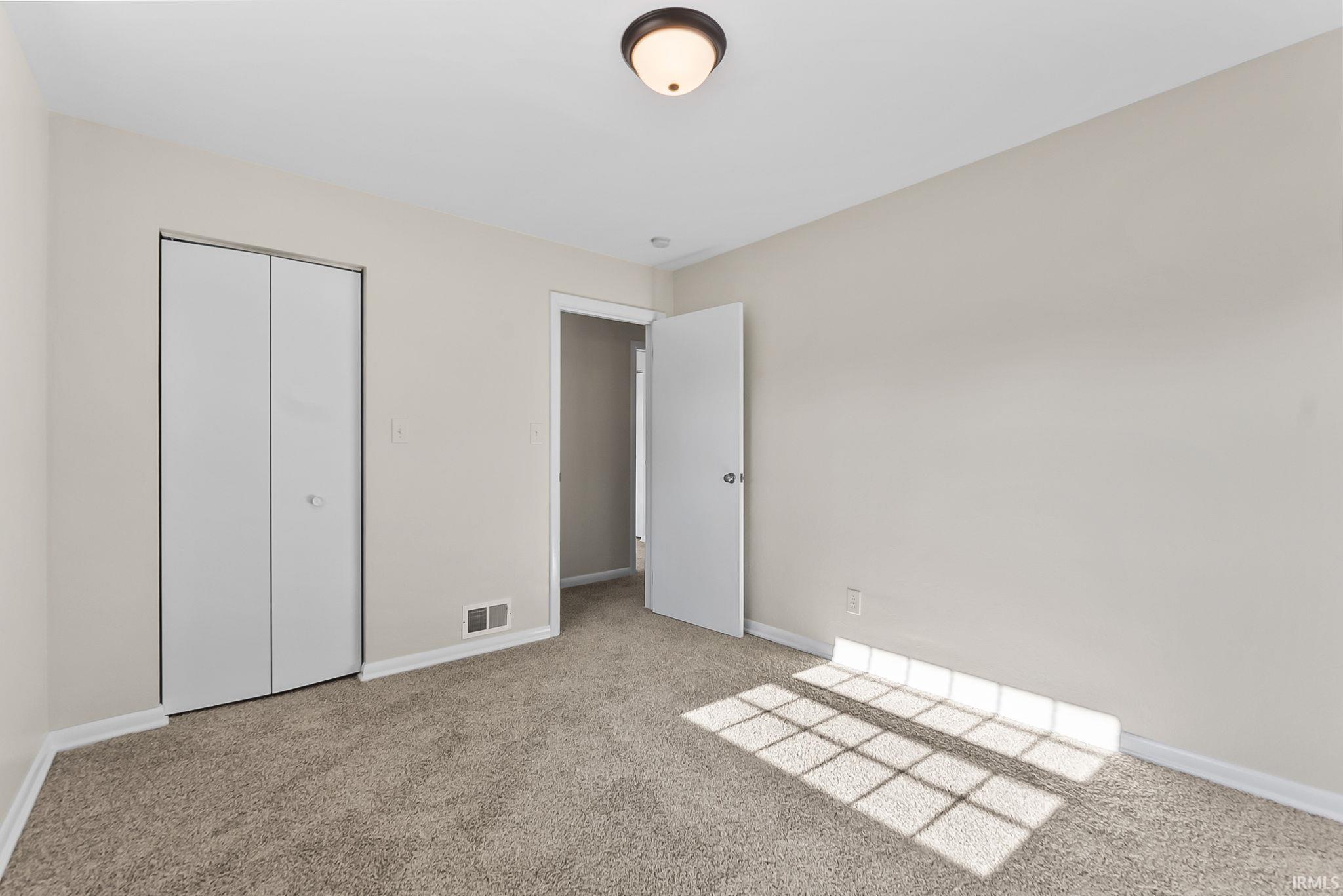 Neutral wall paint, plush carpeting, built-in bi-fold closet, ceiling-mounted light fixture, and a white interior door