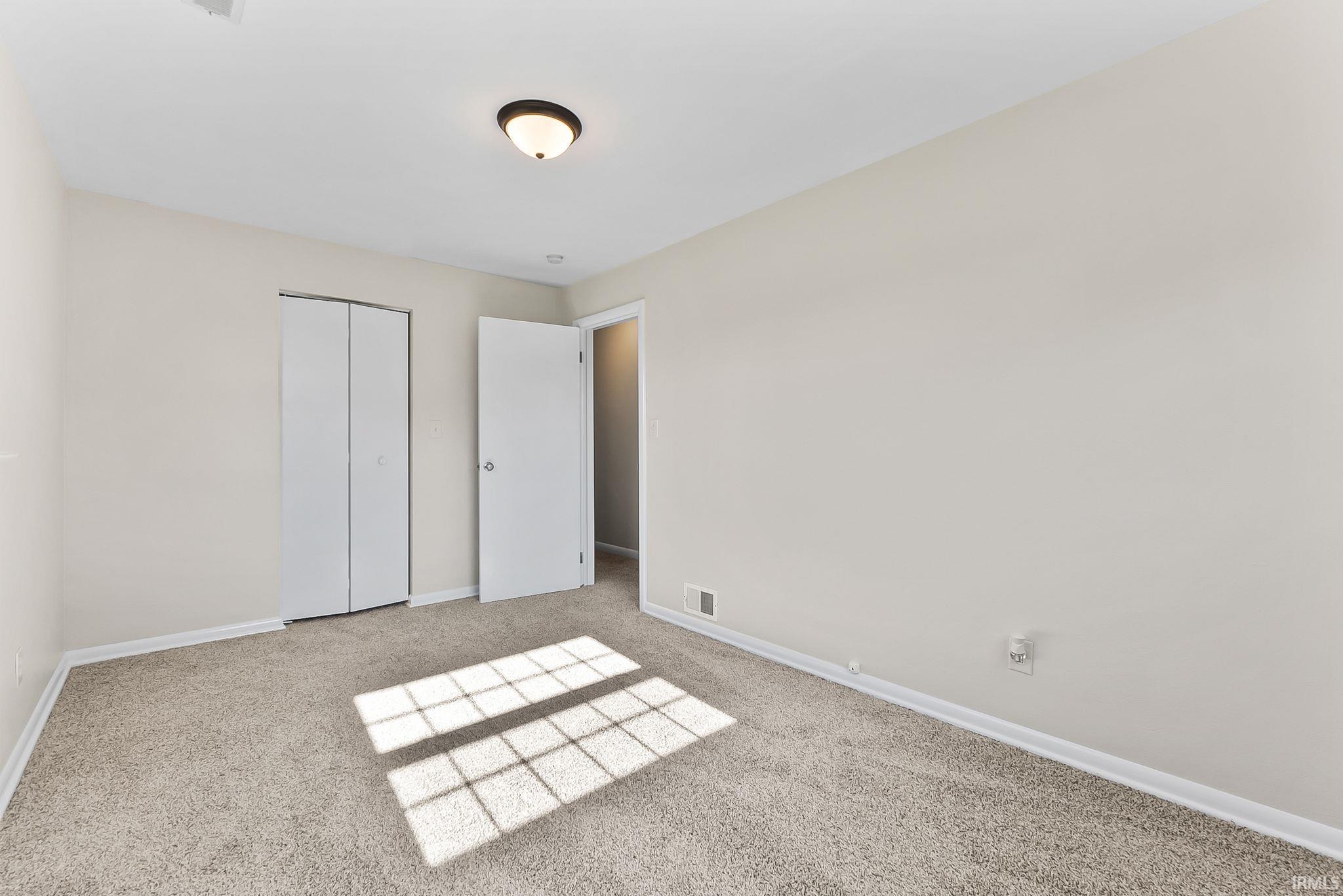 Neutral-toned walls, light-colored carpeting, a ceiling-mounted light fixture, and bifold closet doors