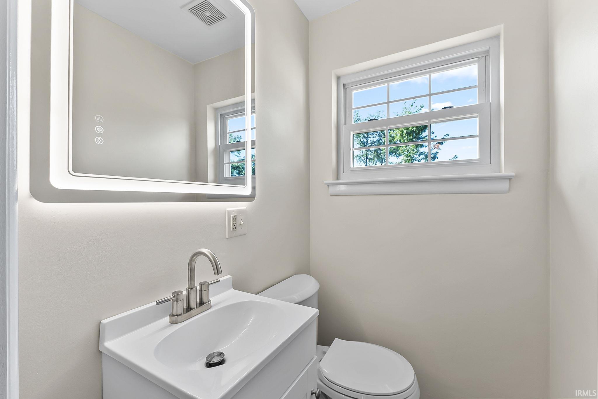 Built-in vanity with integrated sink, brushed nickel faucet, illuminated frameless mirror, and a window with natural light