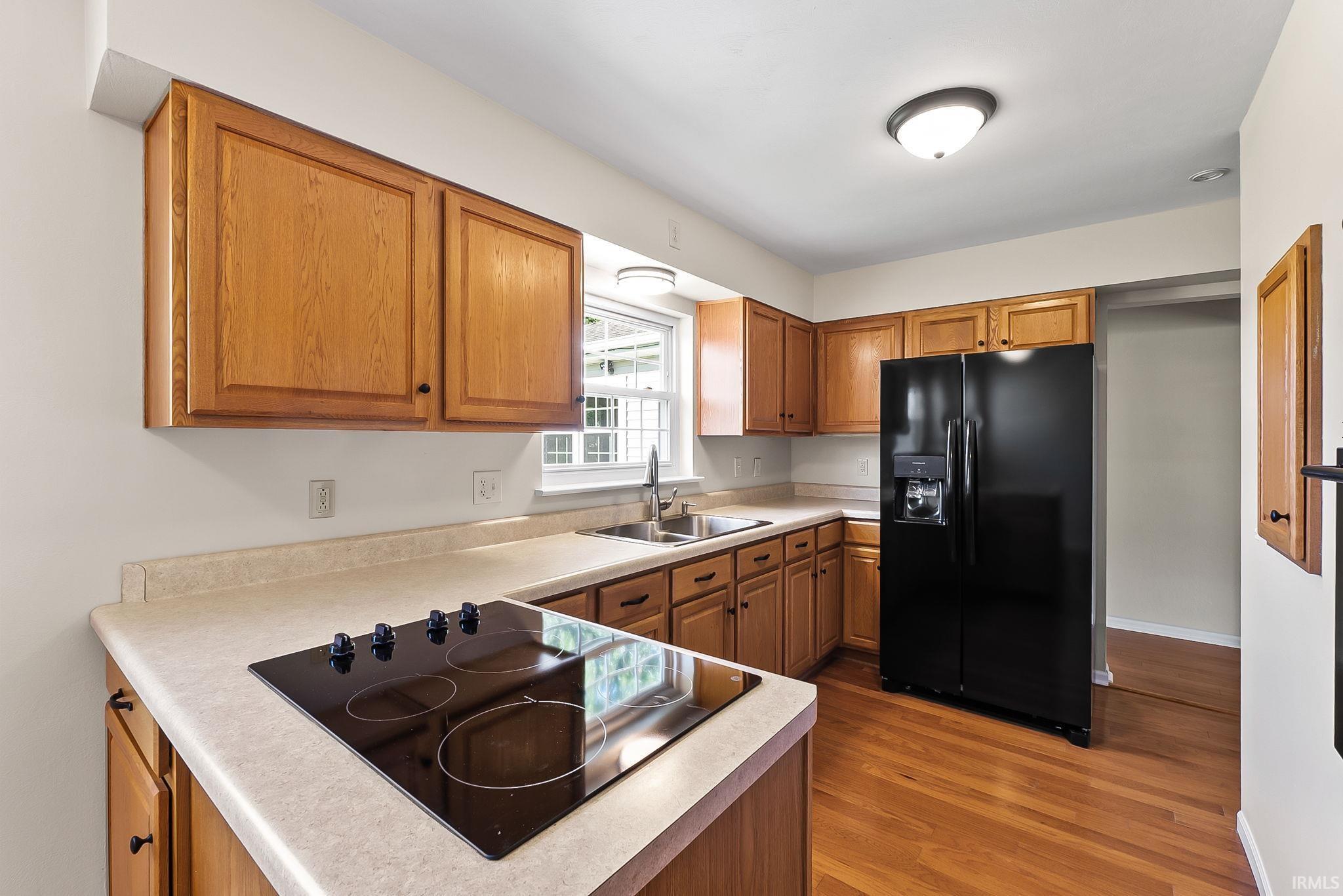 Kitchen featuring wood-finish cabinetry, solid surface countertops, a black electric cooktop, a black side-by-side refrigerator, and wood-finish flooring